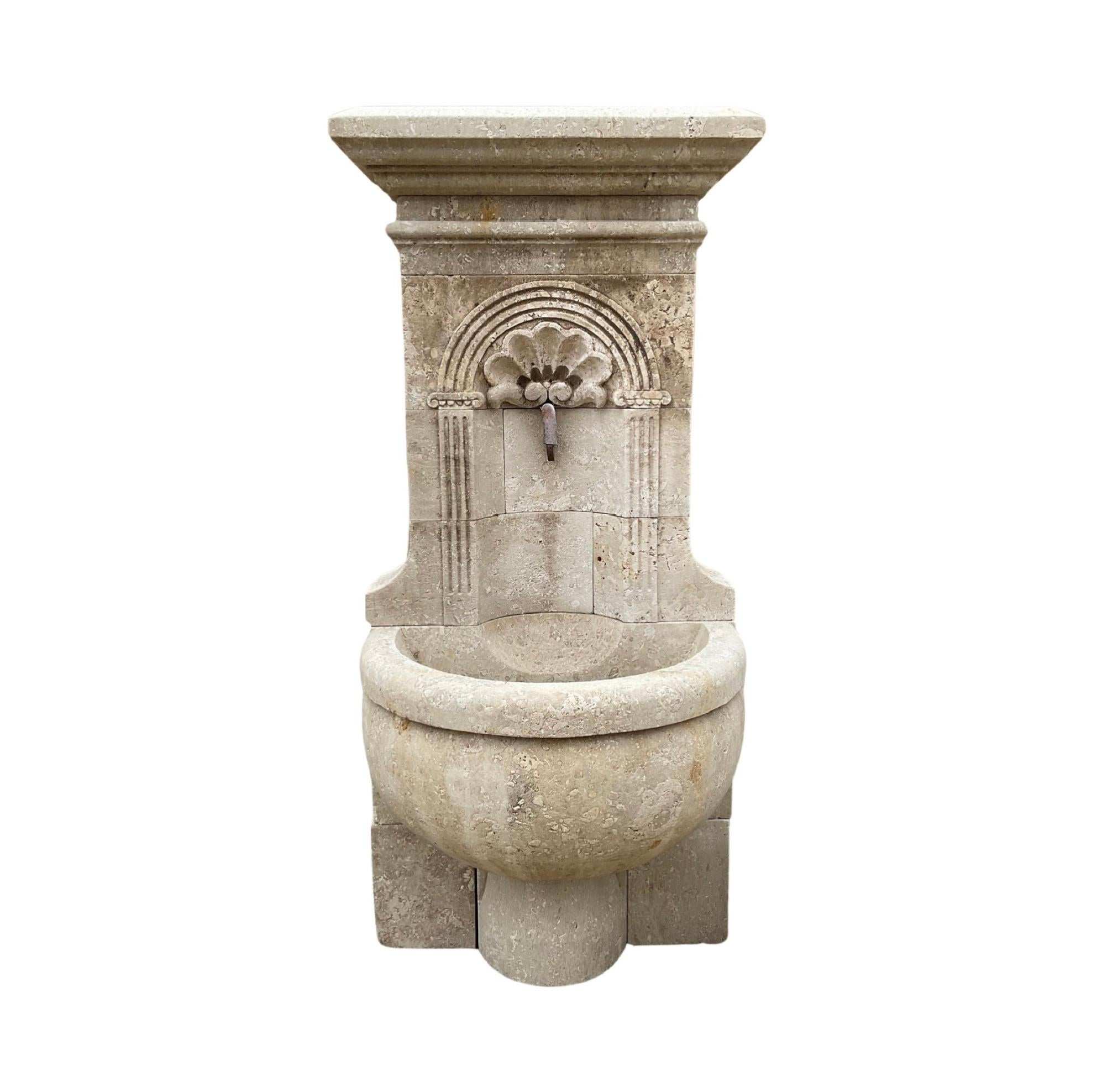 Add a touch of elegance to your space with this 1950s French Limestone Wall Fountain. Made from authentic limestone, its intricate shell-like carvings create a unique and refined look. The semi-circular basin in the front center adds a touch of