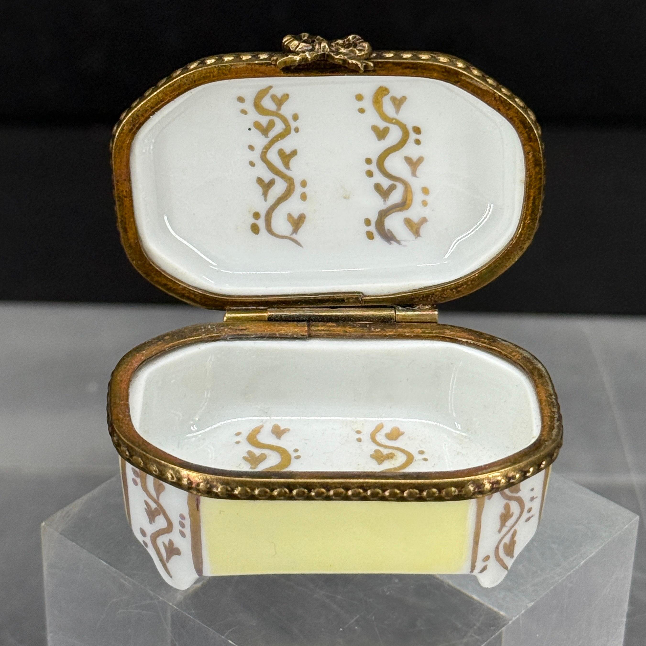 Encontrada en París, una encantadora caja de baratijas de porcelana de Limoges pintada con colores suaves que muestra una escena paisajística con un castillo, un árbol y un velero en el centro. Esta pieza sería sin duda una fantástica adición a una