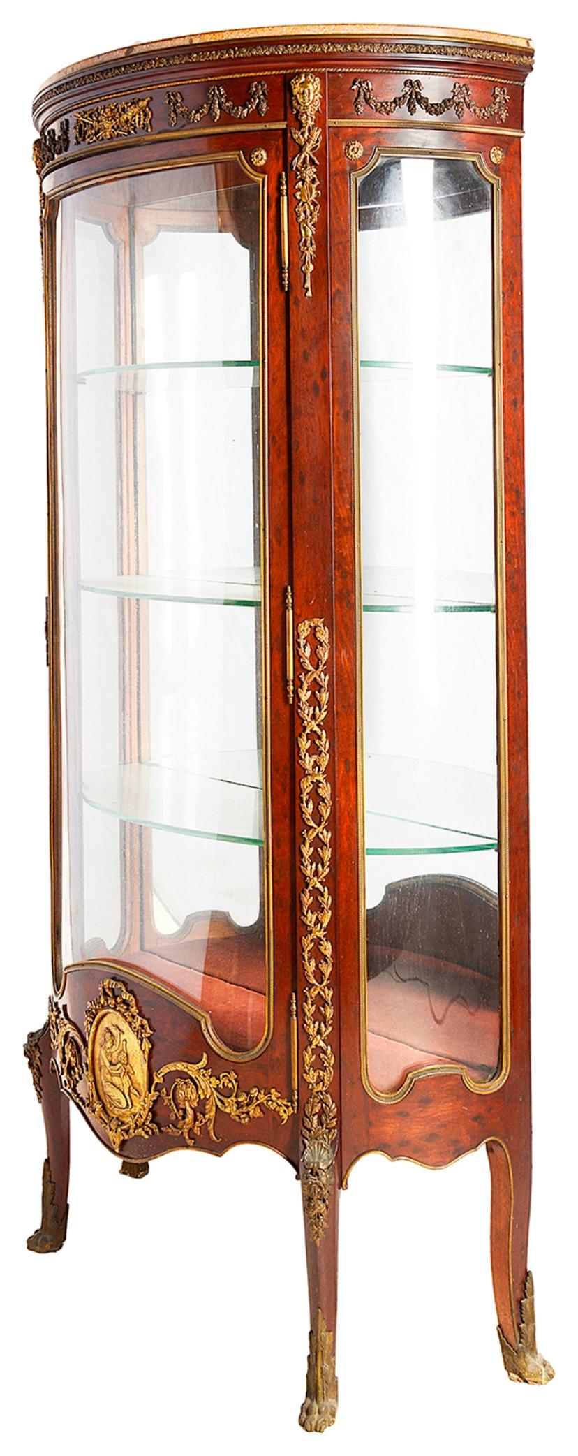 A good quality late 19th century plum pudding mahogany Louis XVI style vitrine, having a marble top, gilded ormolu mounts, shaped glass panels to the door and sides, three glass shelves, mirrored back and raised on elegant out swept feet.