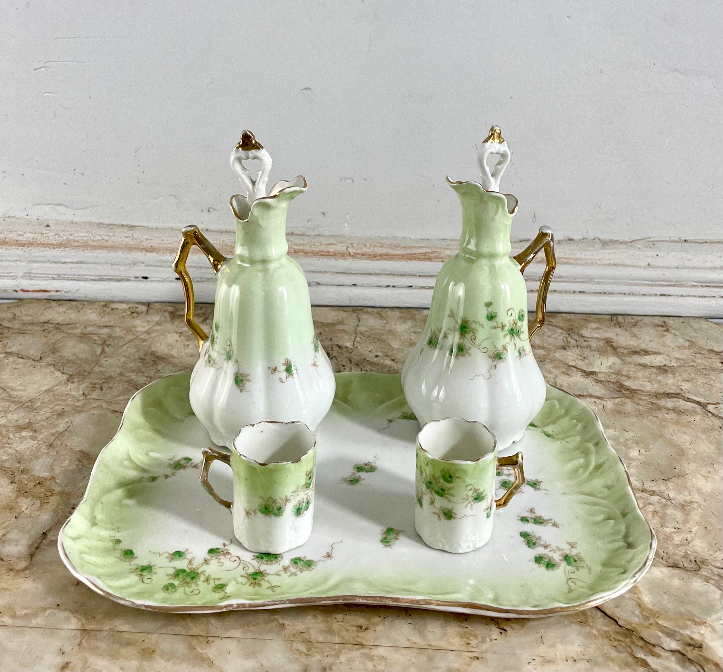 White porcelain liquor service with green and gold floral decoration including an eventful tray, two ewer bottles with their stoppers and two small cups with handles, mugs.
Floral decor. Golden borders and gilding.
French porcelain. Paris