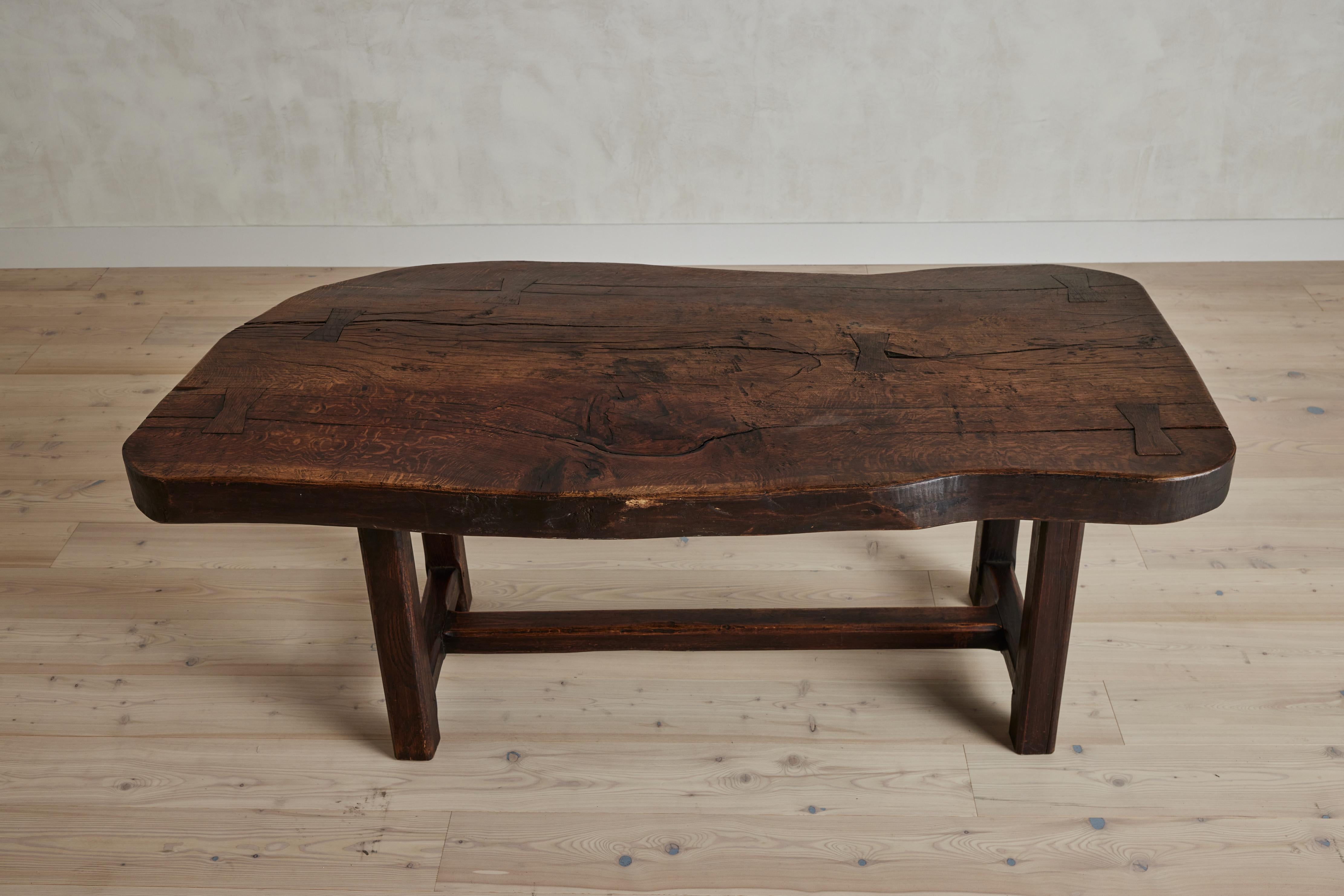 Tobacco hued oak farm table with a rustic live edge detail. France circa early 20th century. Top is slightly bowed. Good vintage condition with some visible wear consistent with age and use. 