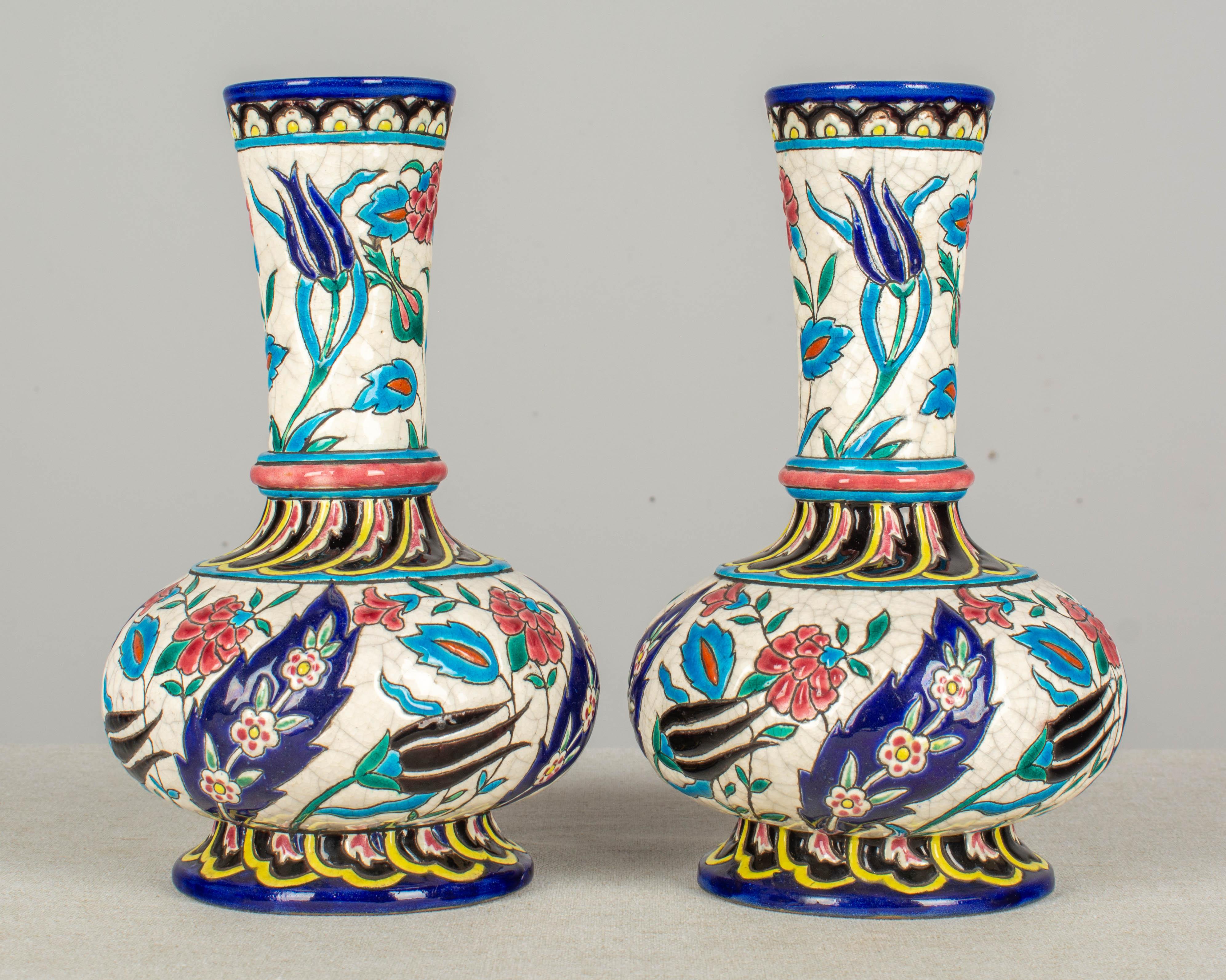 A pair of late 19th century French Longwy enamel cloisonné ceramic bottle form vases. Decorated with hand painted stylized floral and leaf motifs in shades of indigo blue, turquoise, black, rose, green, and yellow on a white crackle ground.