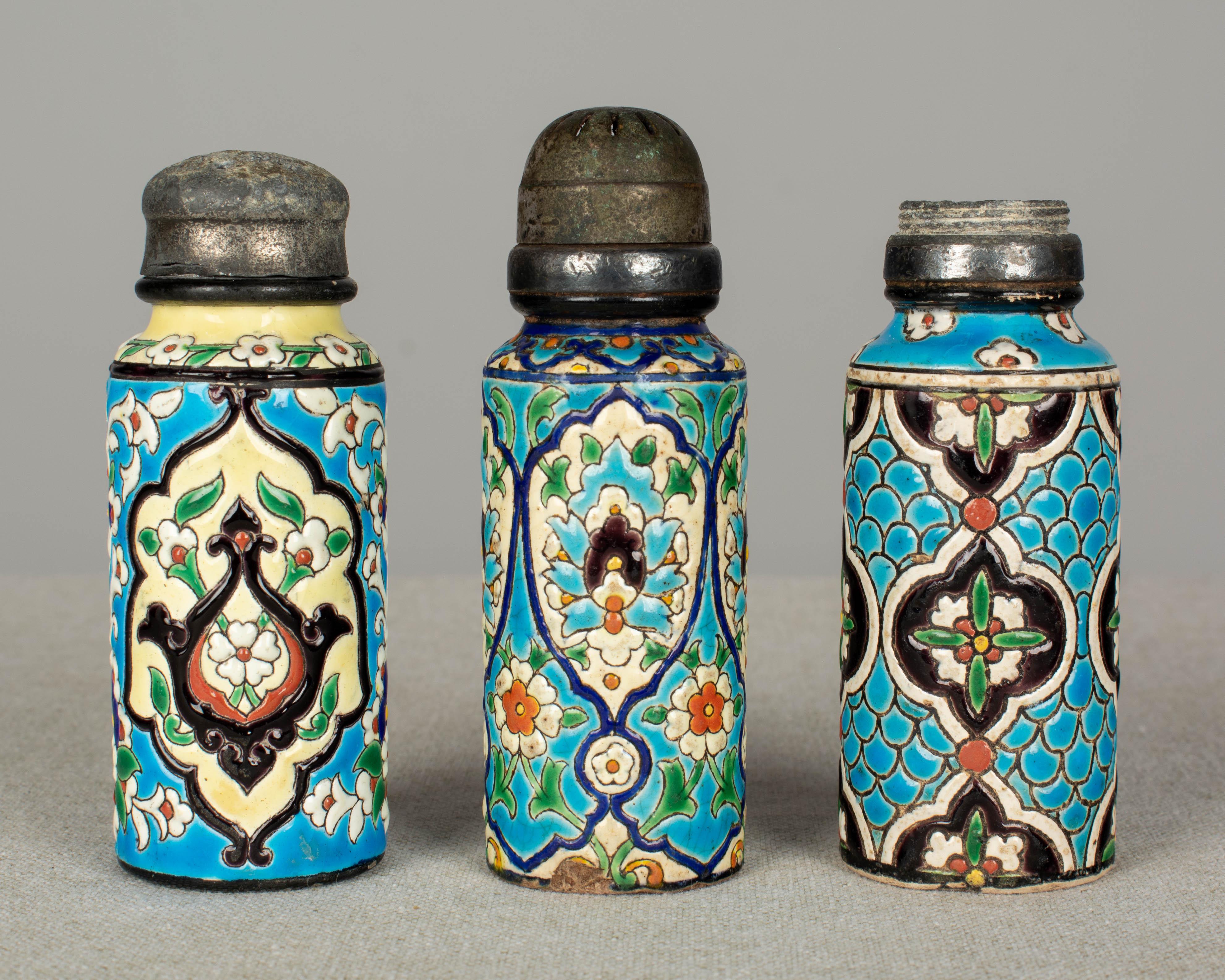 A set of four late 19th century French Longwy enamel cloisonné ceramic shakers. Three salt shakers and one muffiner, or sugar shaker. Decorated with hand painted stylized floral and leaf motifs in bright turquoise blue, orange, green, yellow and
