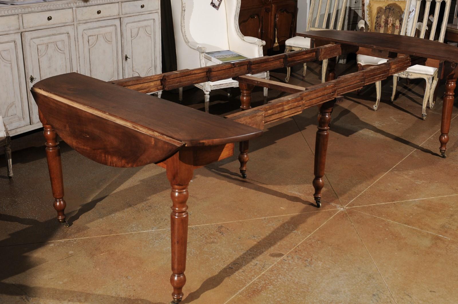 A French Louis-Philippe period oval walnut dining room extension table from the mid-19th century with drop leaves, turned legs and casters. Born in the second quarter of the 19th century during the reign of France's last king Louis-Philippe, this