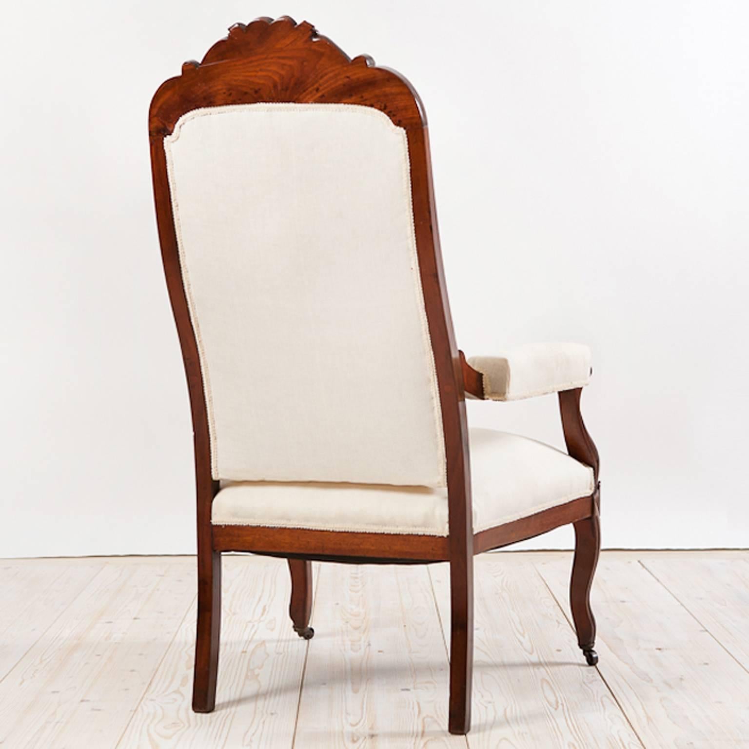 A very handsome Louis Philippe fauteuil in mahogany with carvings of corn flowers & acanthus leaves on crest, with scroll arms and cabriole front legs on casters, upholstered seat, back and padded armrests. The frame of this armchair has been