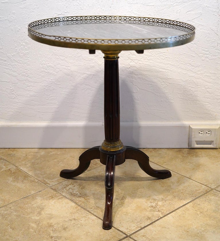 This elegant French Louis Philippe gueridon table features a grey marble top surrounded by an openwork bronze gallery and resting with a tilt top mount on a fluted pedestal, the lower part with double fluting. A circular bronze mount attaches the