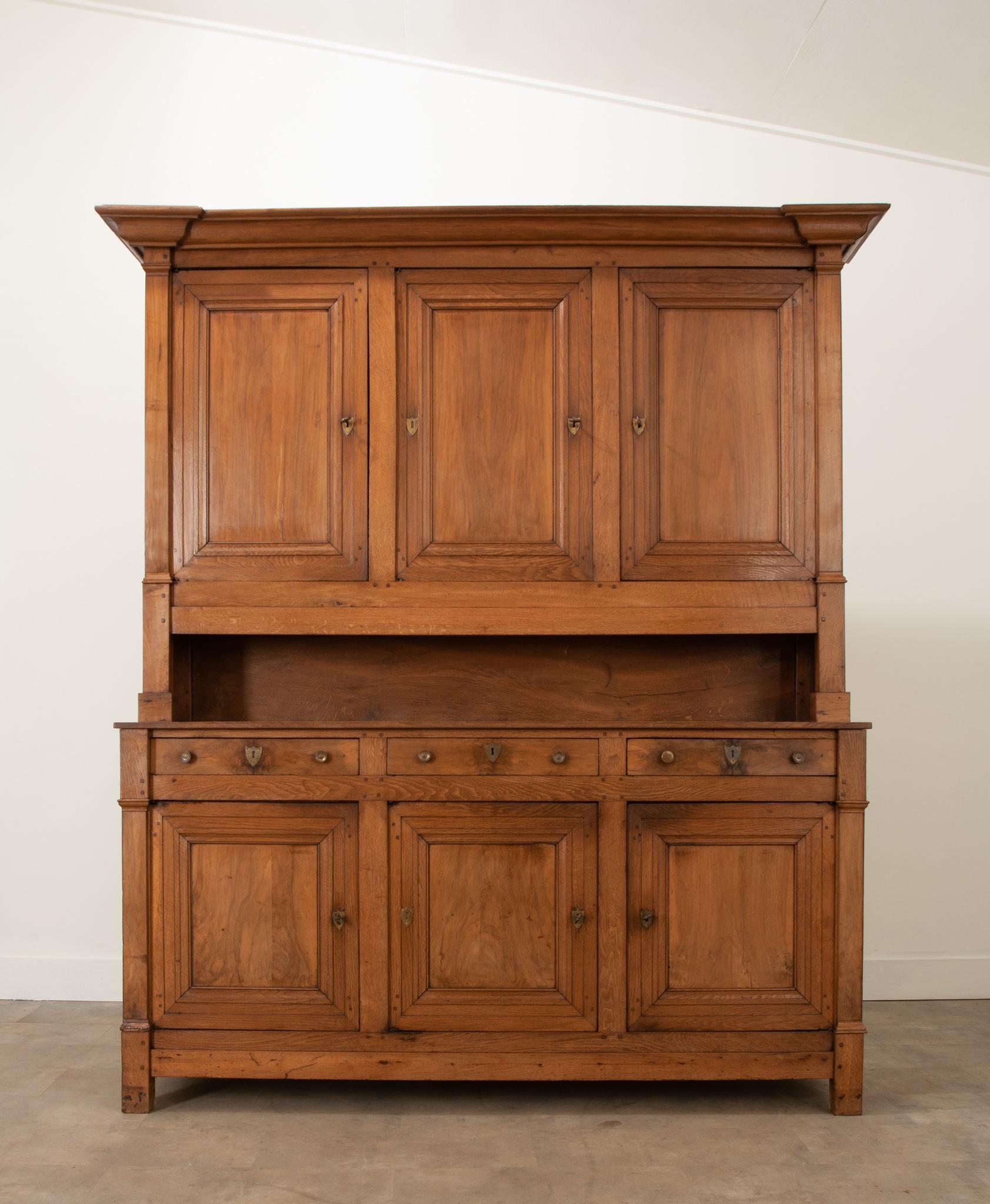 A charming solid oak buffet a deux corps crafted in France during the 19th century. A large molded cornice sits over the top of three paneled doors and are all fixed with shield shaped escutcheons. They all open to a single storage cavity with two