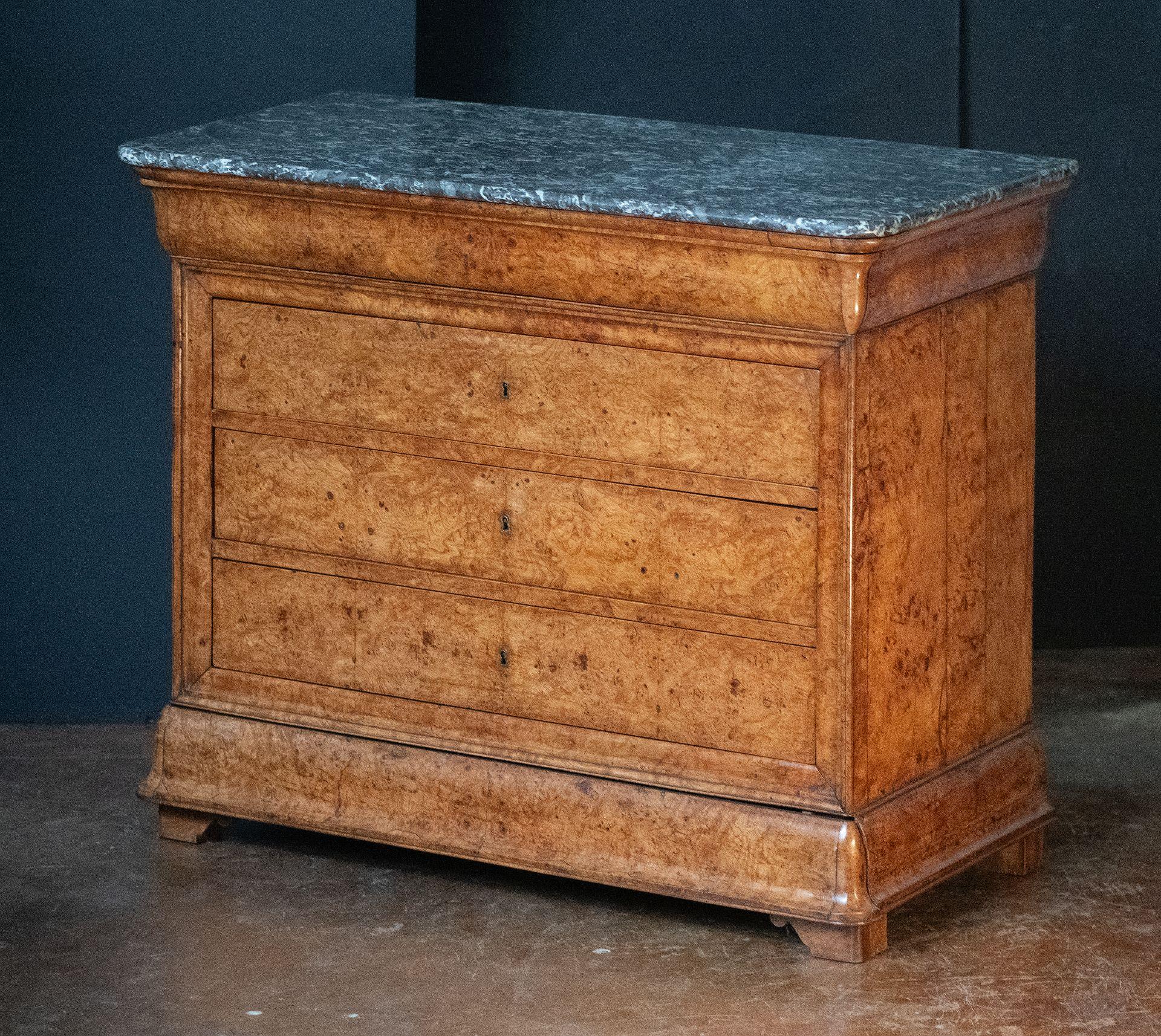 A fine Louis Philippe console chest or commode from France, with veneers of beautifully patinated burled ash with a rectangular figured marble top, featuring a frieze of five drawers - three middle drawers with escutcheons, and two as fitted