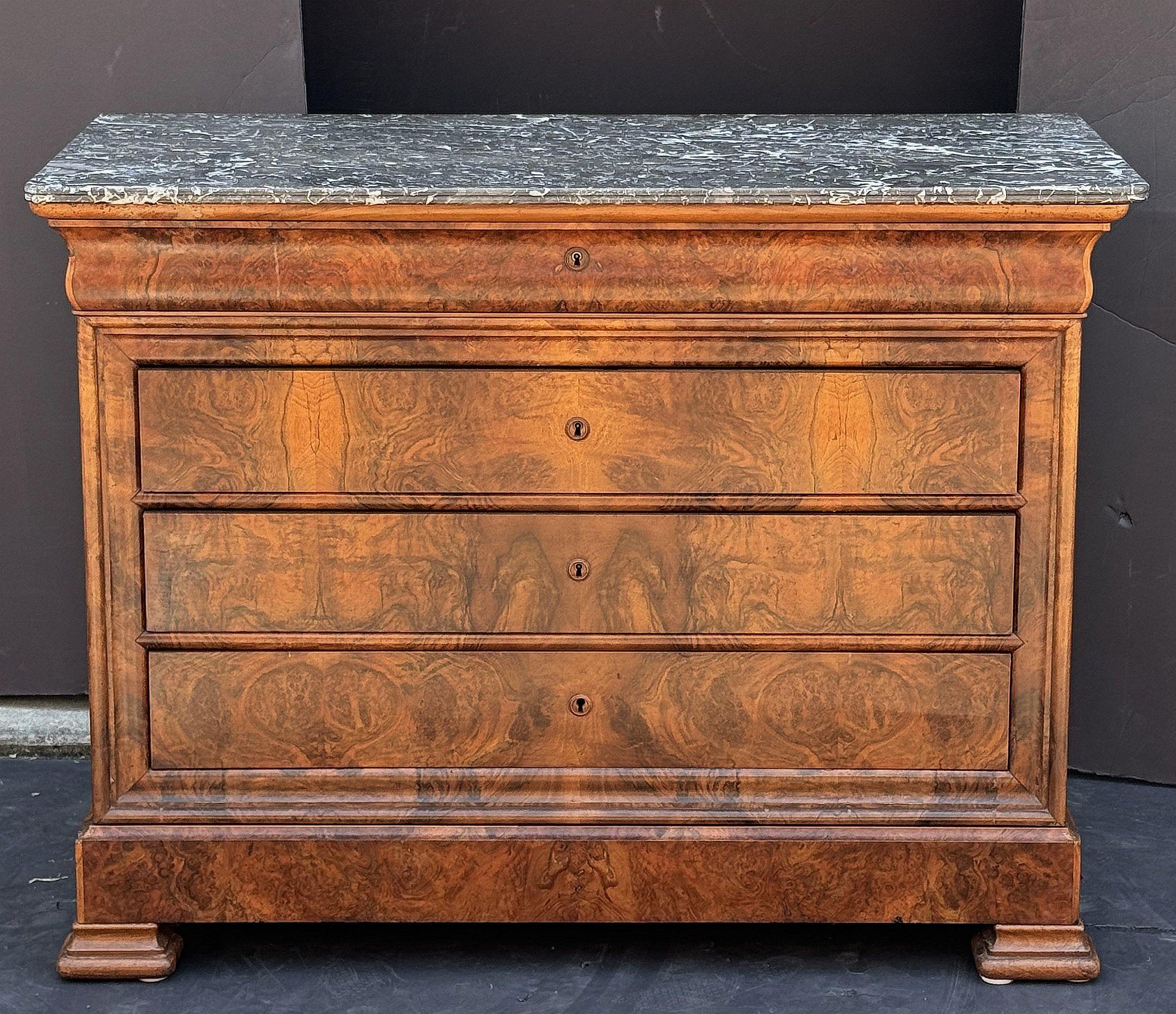 A fine Louis Philippe console chest or commode from France, of beautifully patinated burled walnut with a figured marble top, featuring five fitted long drawers, brass escutcheons, and set upon shaped feet.