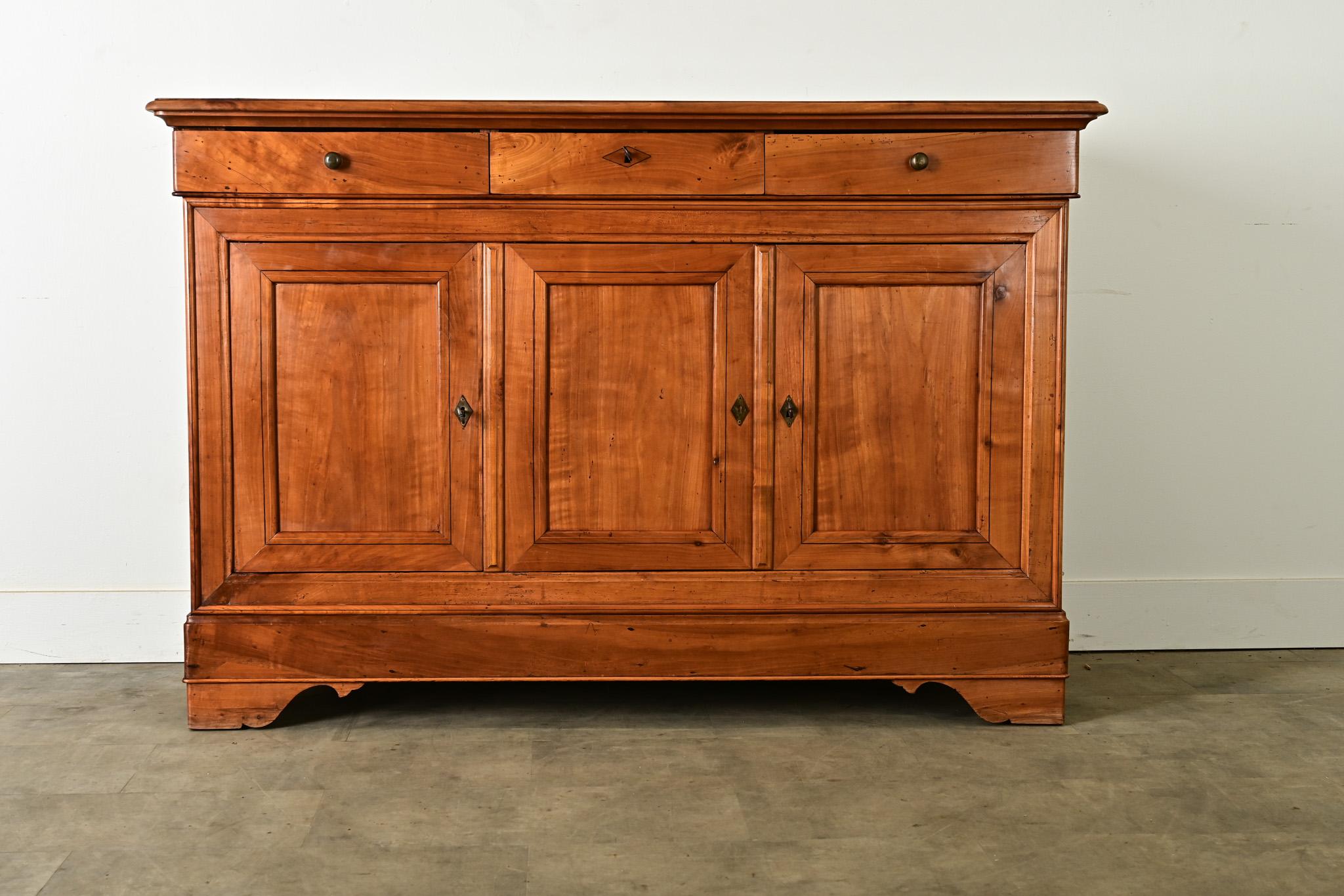 Une belle enfilade du XIXe siècle, d'époque Louis Philippe, fraisée et sculptée dans du bois fruitier. Les planches lisses du plateau sont disposées en planche à pain, ce qui met en valeur la beauté du grain. Dans la frise se trouvent trois tiroirs