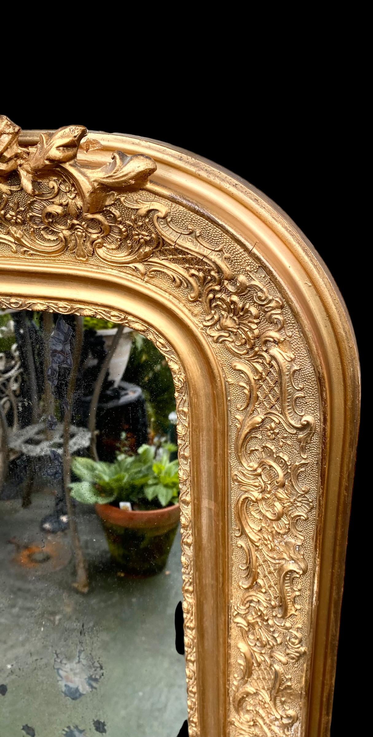 French Louis Philippe Gilt and Gesso Overmantel
Mirror, 19th century, with a pierced scroll and relief floral crest above a wide rounded corner frame with relief floral and scroll decoration around an arched top mirror plate. 

Antique French