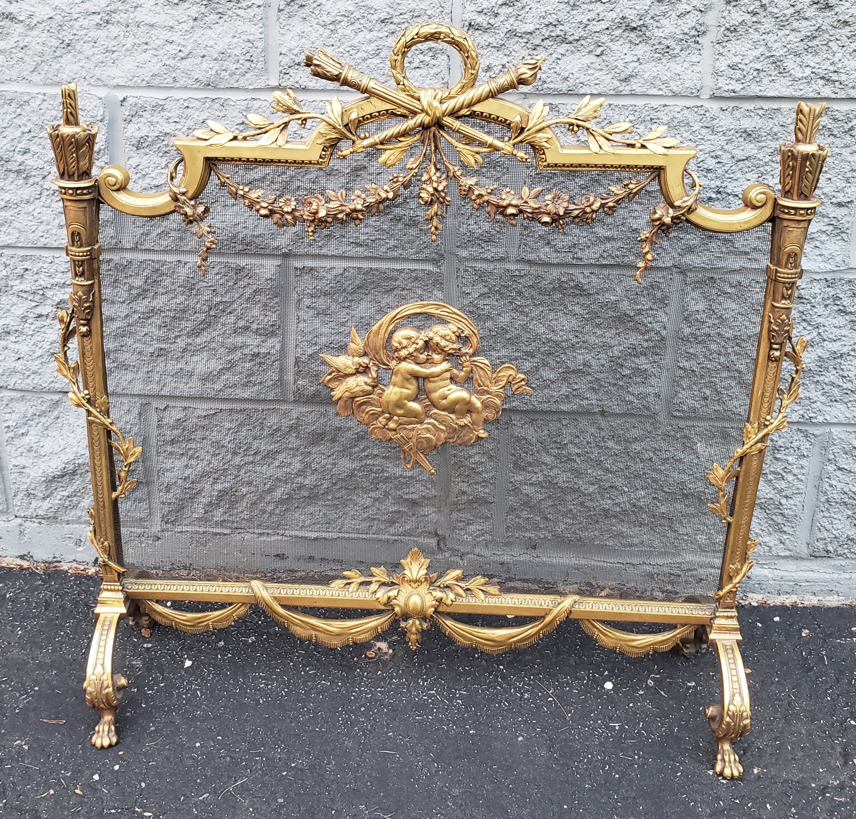 French gilt bronze cherub and decorative floral acanthus.
French gilt bronze freestanding fire screen with centered Cherubs medallion and torch handle, flanking acanthus finials, lowered ribbon swags and floral scroll work, lower cartouche with