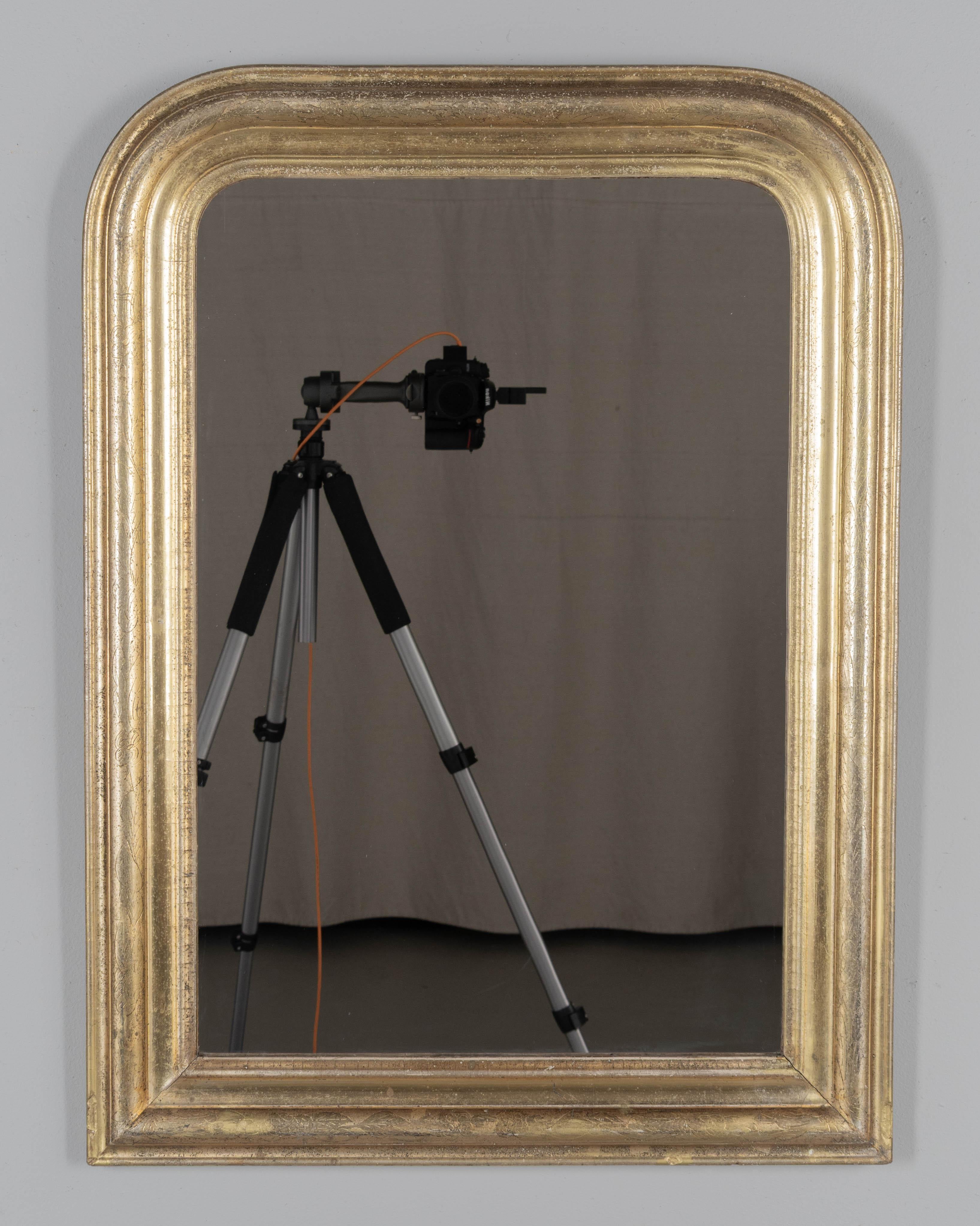 Miroir français de style Louis Philippe du début du 20e siècle, avec des angles supérieurs incurvés, une décoration florale incisée et une finition dorée brillante. Miroir original. Deux planches de bois à l'arrière sont remplacées. Veuillez vous