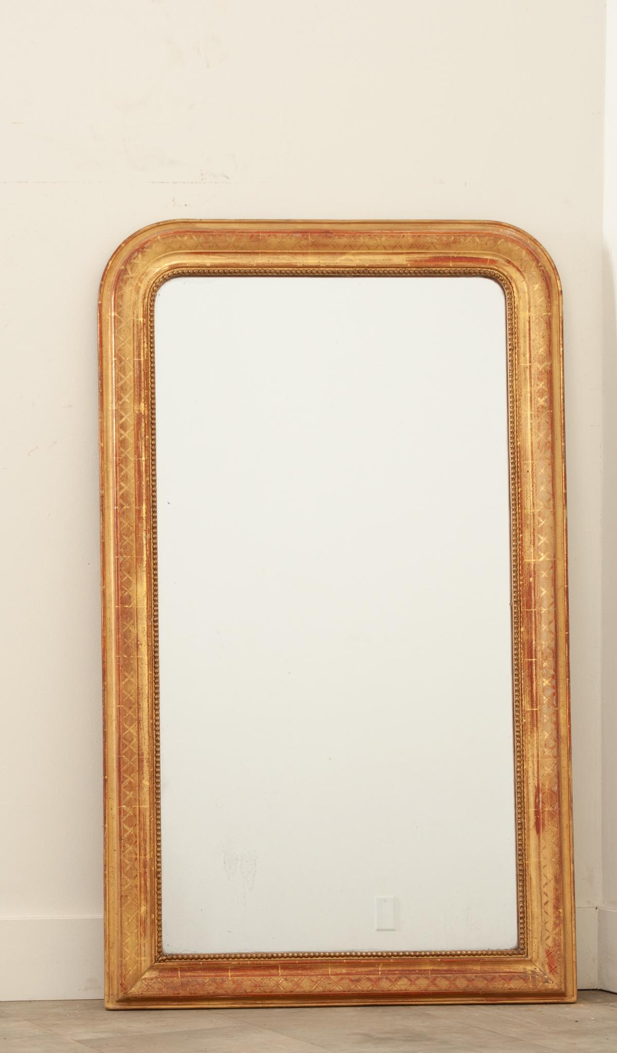 This French Louis Philippe style mirror hand-crafted in France in the 19th century is elegant and timeless with its molded and trimmed rectangular frame with rounded top corners. This lovely mirror features a beautifully etched cross hatch pattern