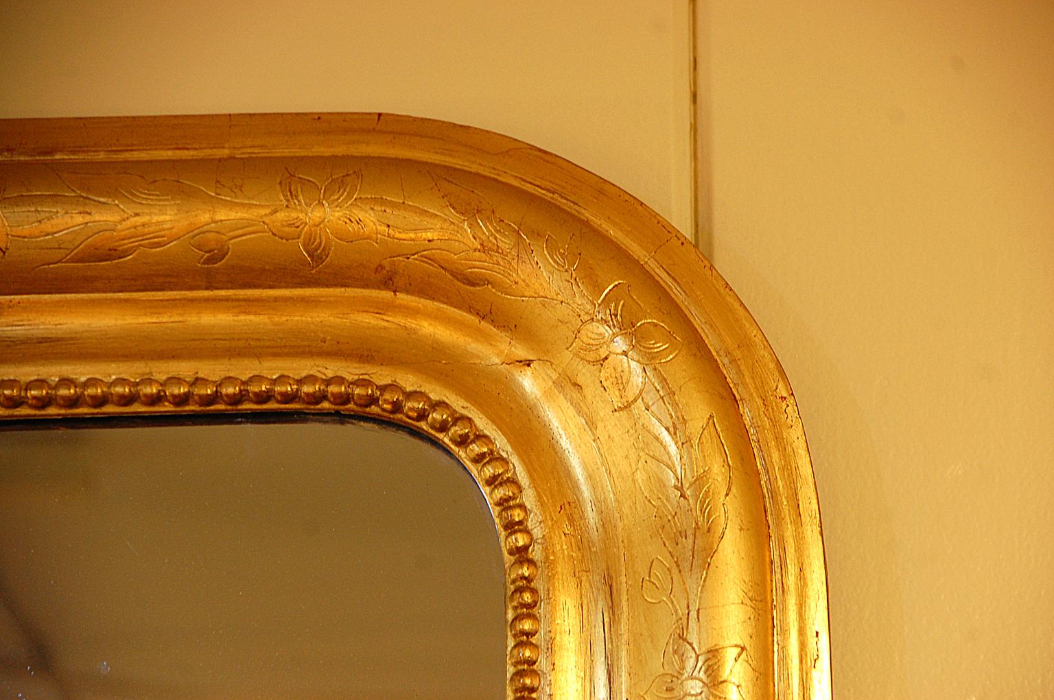 French Louis Philippe gold leaf on wood and gesso incised 54 inch tall mirror. The molded frame has been incised with subtle floral decoration, the mirror is original with flaws as is usual in original mirrors, but it is not bothersome, rather it