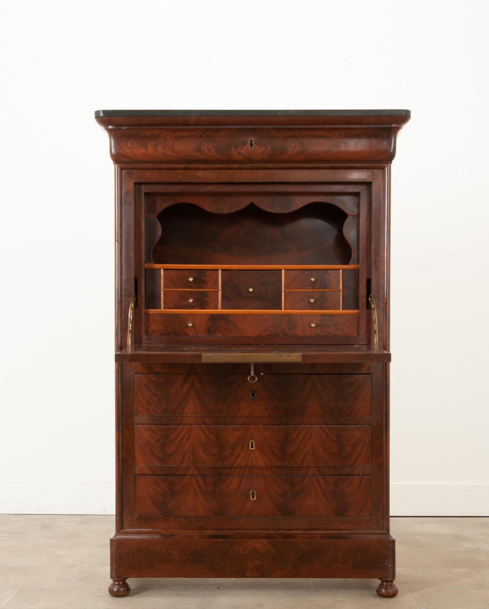 A handsome French 19th century bookmatched mahogany secretaire á abattant with a black marble top. A single drawer can be found at the top of the desk above a fold down writing surface, when unlocked this reveals a hand-carved scalloped design,