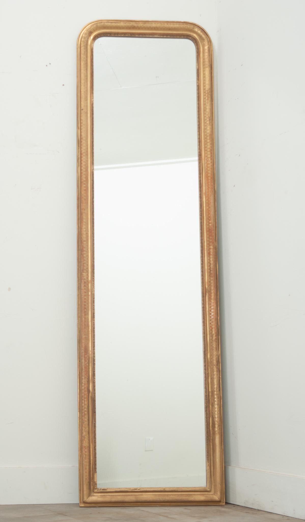 Miroir de coiffeuse Louis Philippe, haut et étroit, fabriqué en France. La dorure d'origine du cadre présente une certaine patine, l'usure naturelle ayant révélé la couche de base rougeâtre du bole et créé un contraste unique avec la finition dorée.