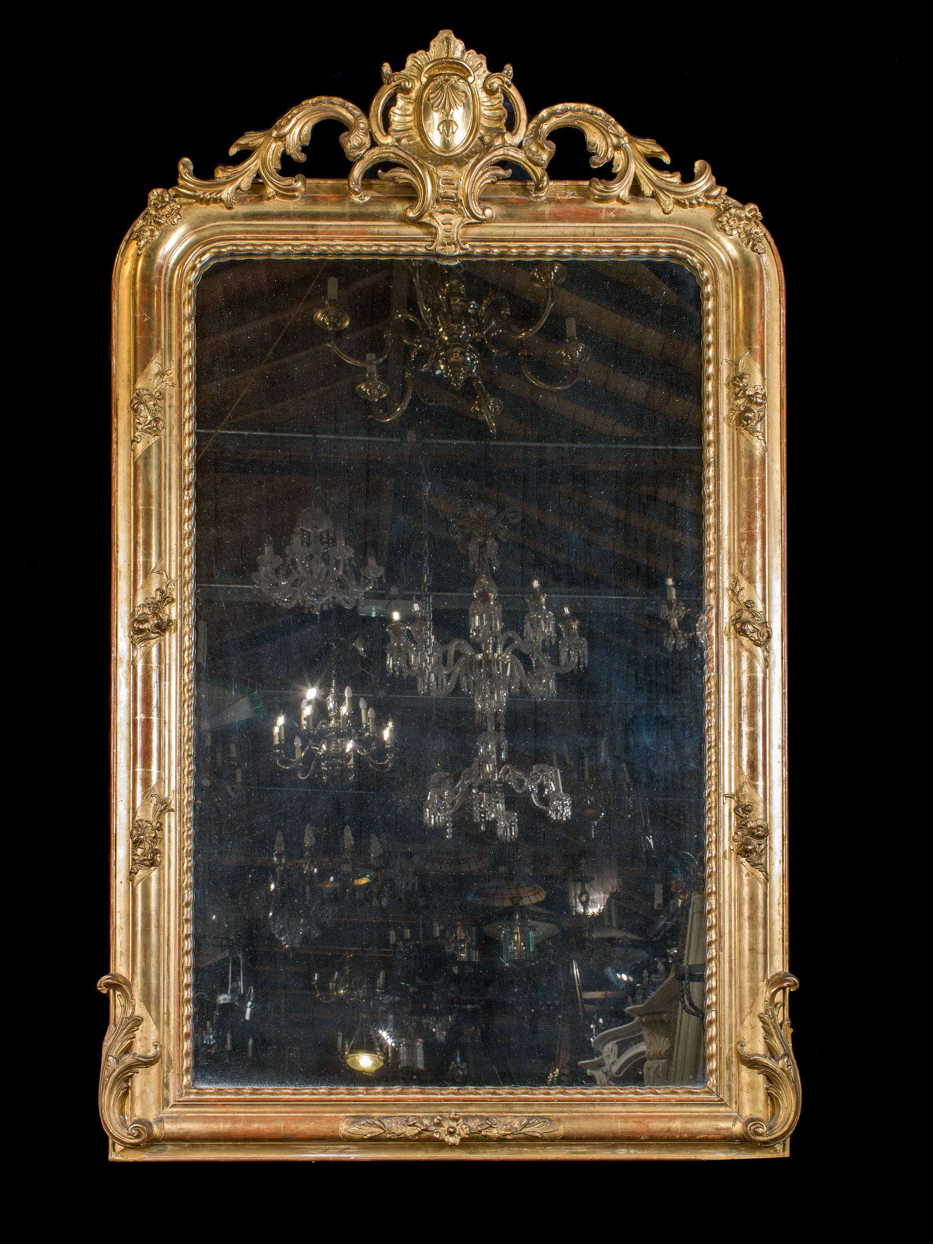An elegant French 19th century giltwood overmantel mirror in the Louis Philippe style, surmounted by a cartouche of rocaille design mounted above rounded corners. The frame has been beautifully gilded and is embellished by a floral ribbon design