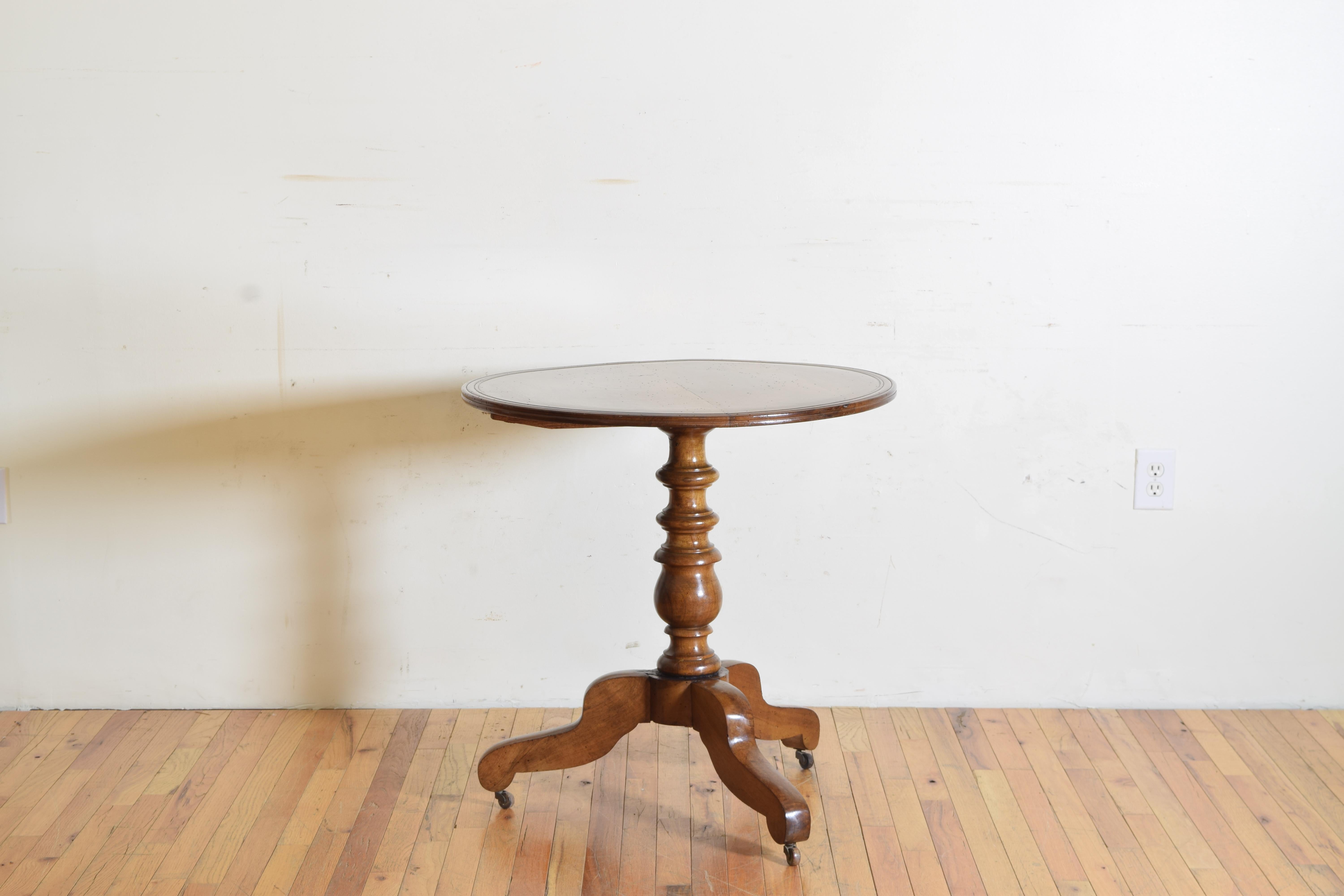 The round top with galleried edge resting atop a turned standard with removable tilt controlling hand shaped pin supported by a tripartite base with antique brass casters.