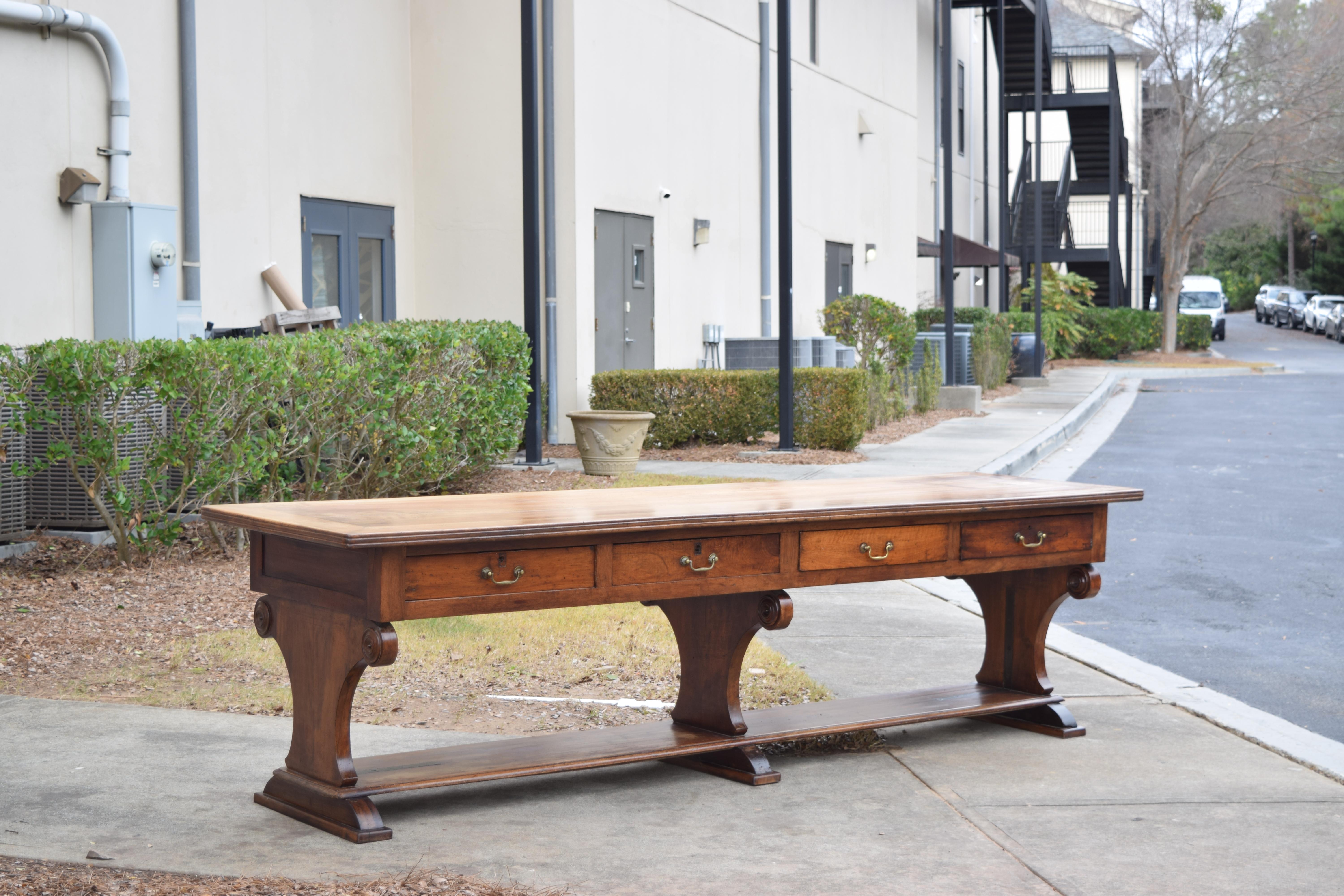 constructed entirely of solid walnut, the two board top is bookmatched and has a triple molded edge for alignment of scissors, the case housing four drawers and finished around to float, raised on three trestle-form supports, the end with turned