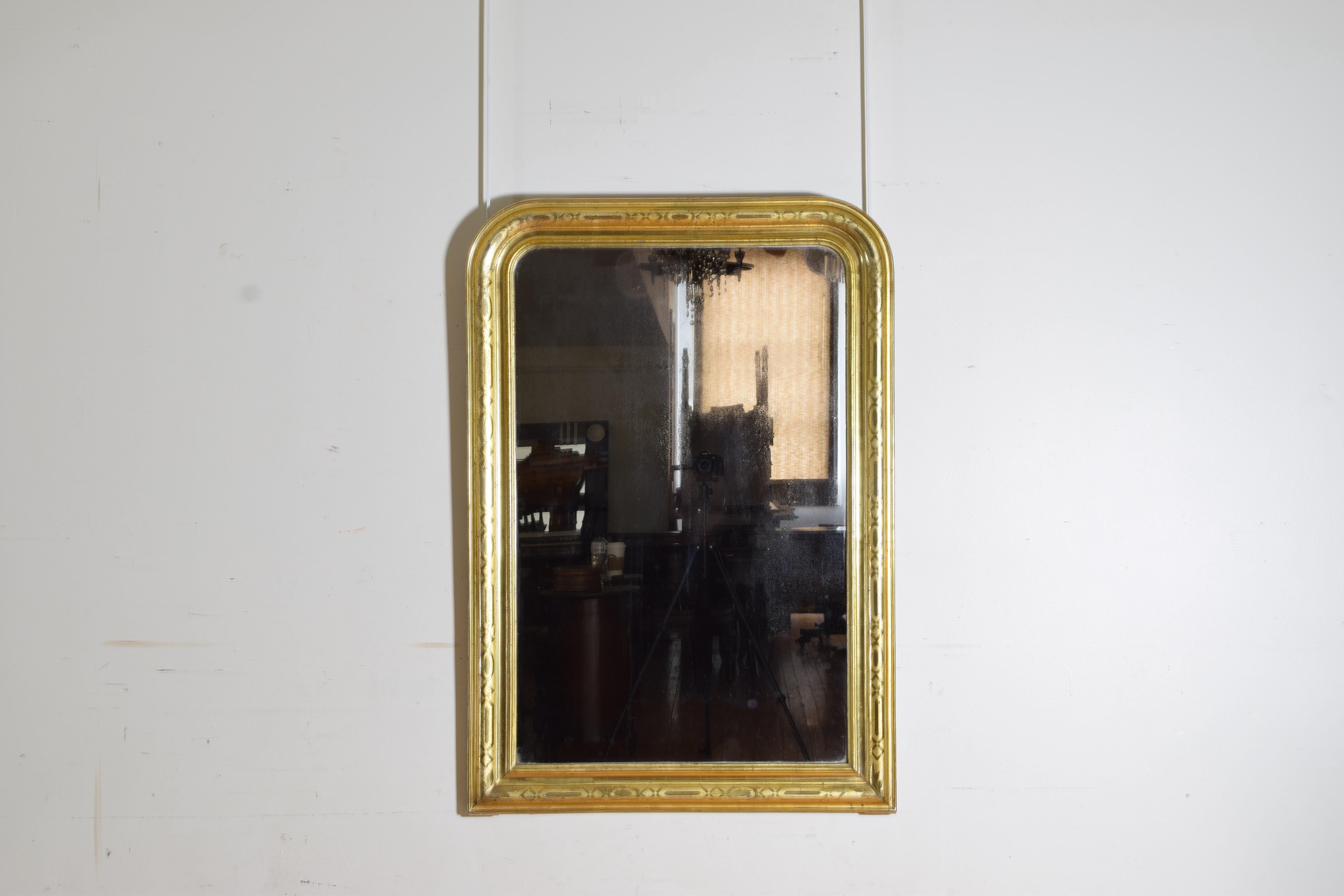 The rectangular frame with rounded top corners with raised moldings creating layers the highest molding with lozenge and oval shaped stencils of 23k gold, retaining original mirror plate and wooden backing, second quarter of the 19th century.