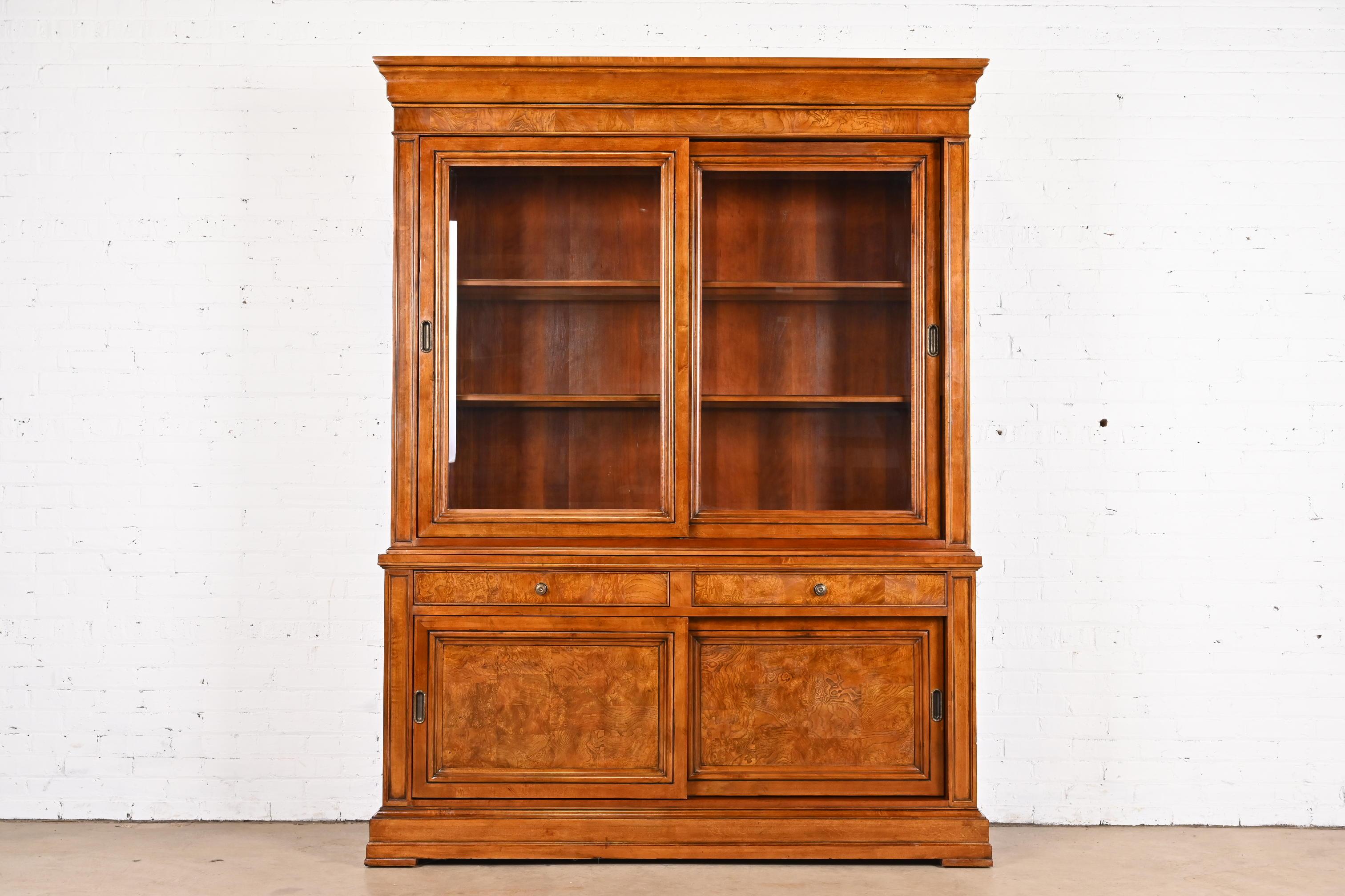 A gorgeous French Louis Philippe style two-piece lighted breakfront bookcase or display cabinet

USA, Circa 1990s

Burl and cherry wood, with glass front doors and original brass hardware.

Measures: 66.75