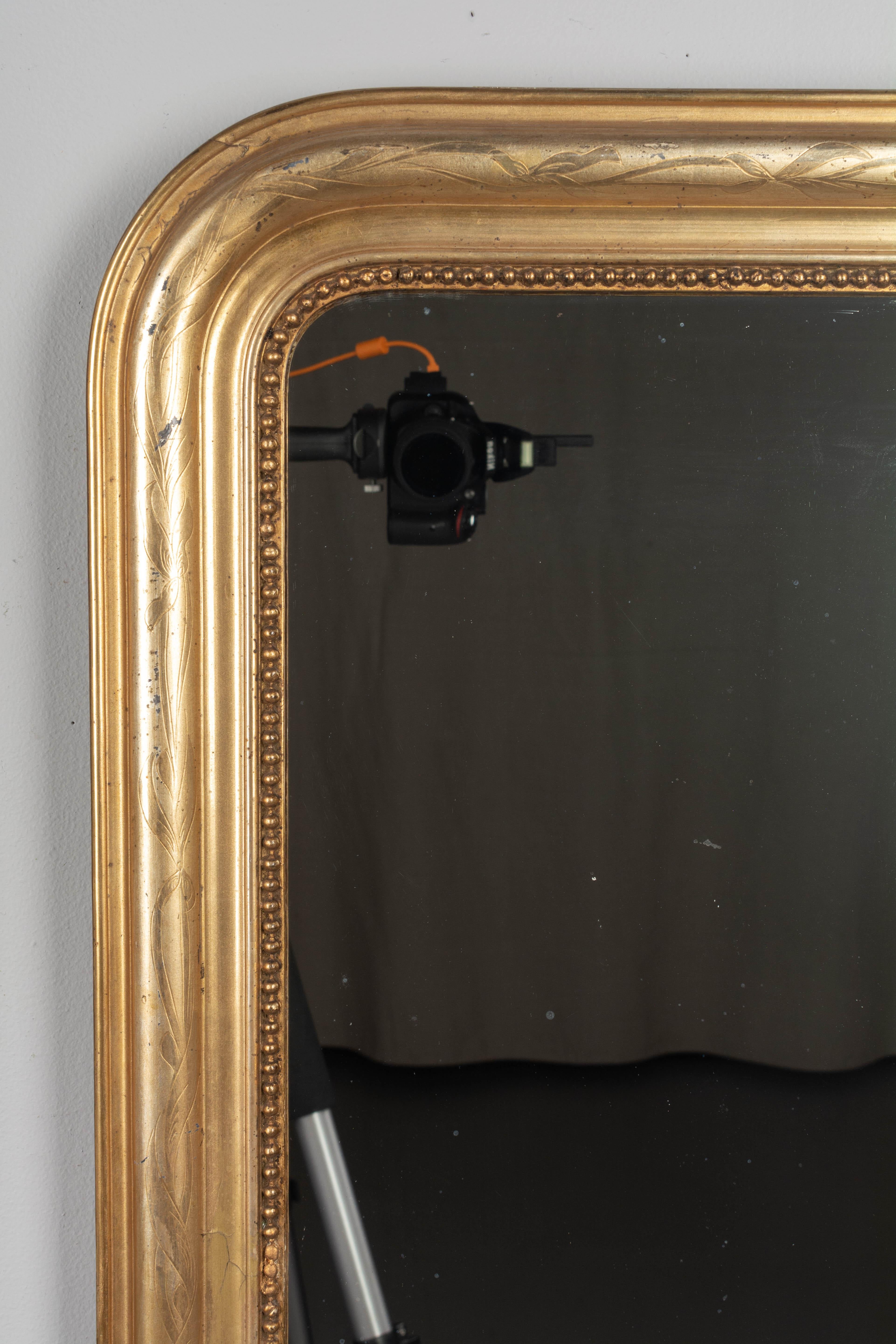 A French Louis Philippe style gilded mirror with curved top corners, incised decoration and inner bead border. Warm gilt finish. Original mirror. Frame has been restored on the upper right edge and bottom corners. Some touch-ups to gilt. Please