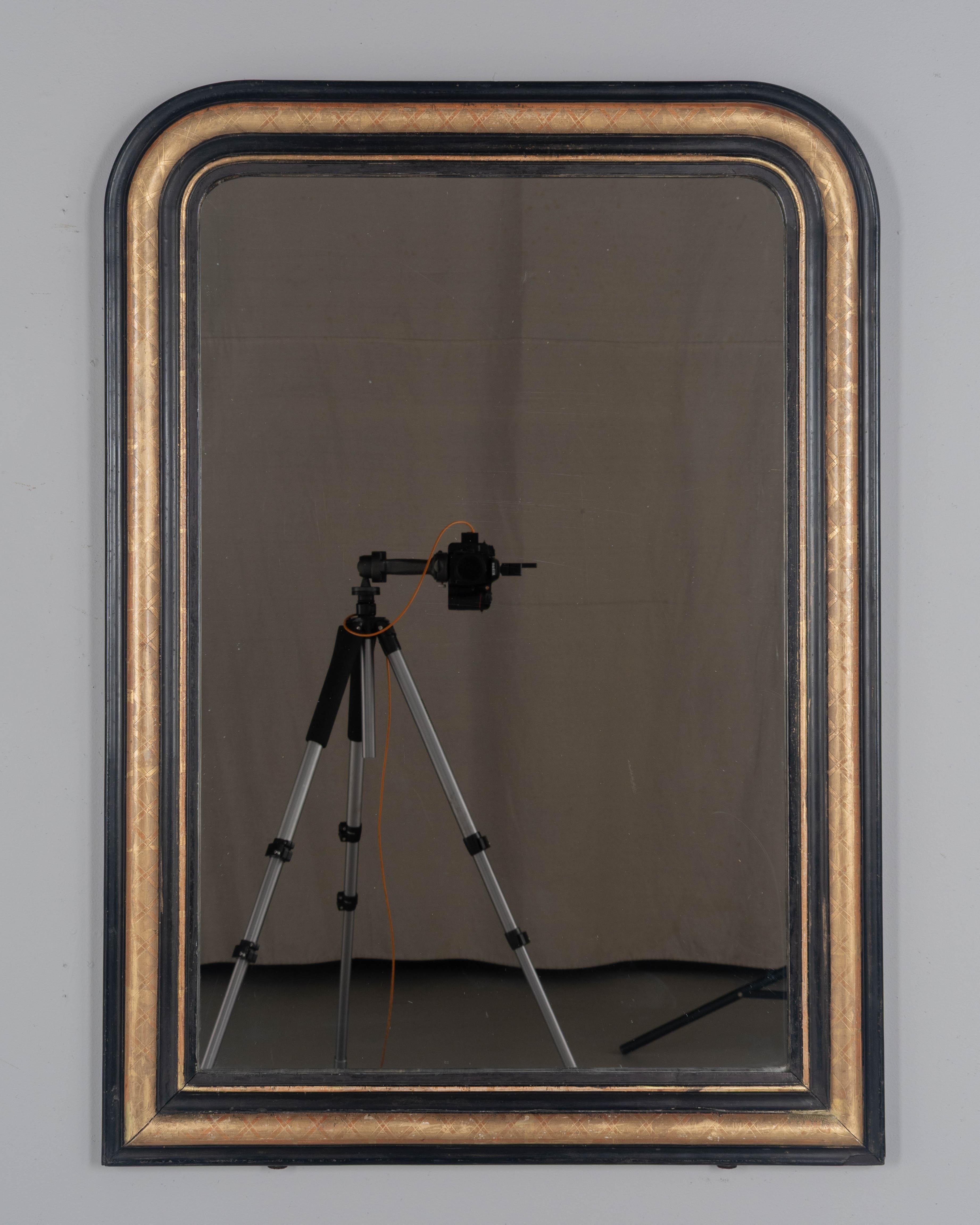 An early 20th century French Louis Philippe style gilded mirror with curved top corners, incised x pattern. Black painted inner and outer border and beautiful gilt patina with red under rub exposed. Original mirror. Frame has been minimally restored