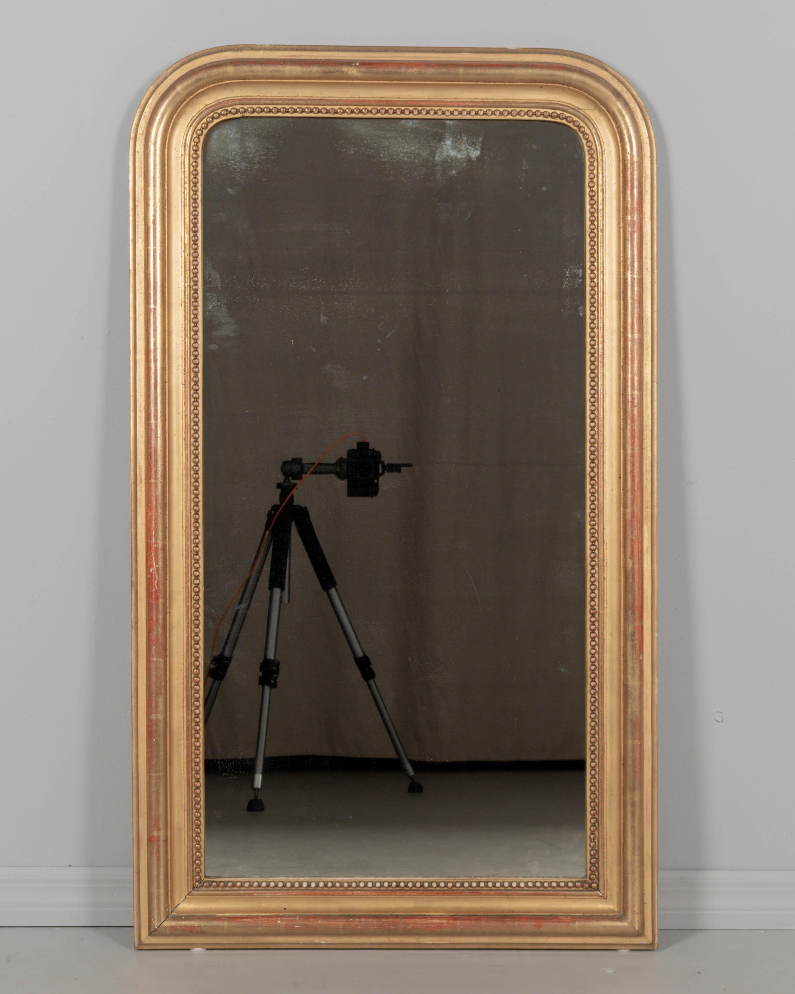 An early 20th century French Louis Philippe style mirror with curved top corners and inner bead border. Bright gilt finish with red clay under rub. In very good condition with minor losses and touch-ups. Stamp on back: Marly Miroitier a Bordeaux.