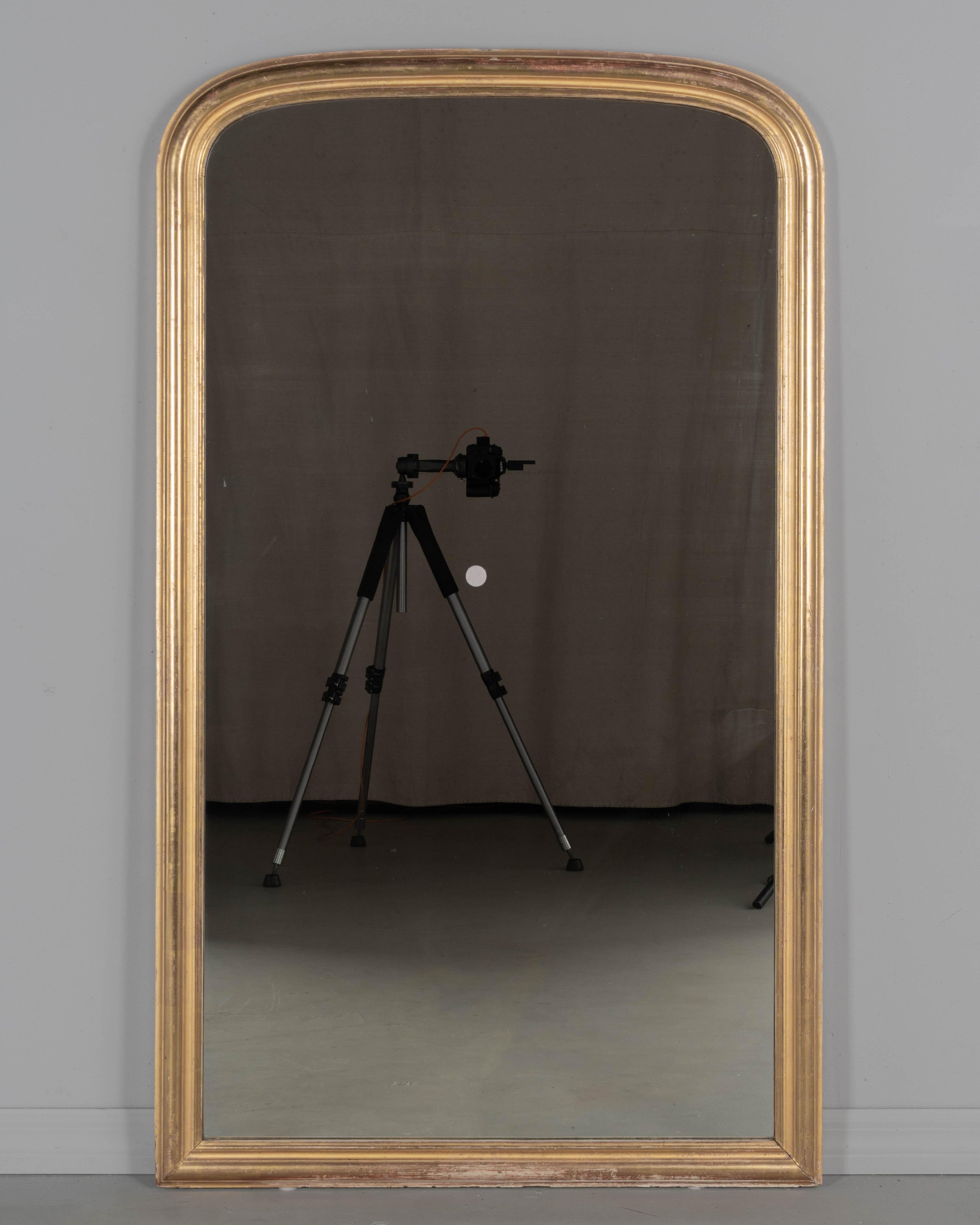 An early 20th century French Louis Philippe style mirror with elegant proportions and slightly curved top corners. Slim molding with bright gilt finish and red clay under rub. In very good condition with minor losses. Original mirror is in good