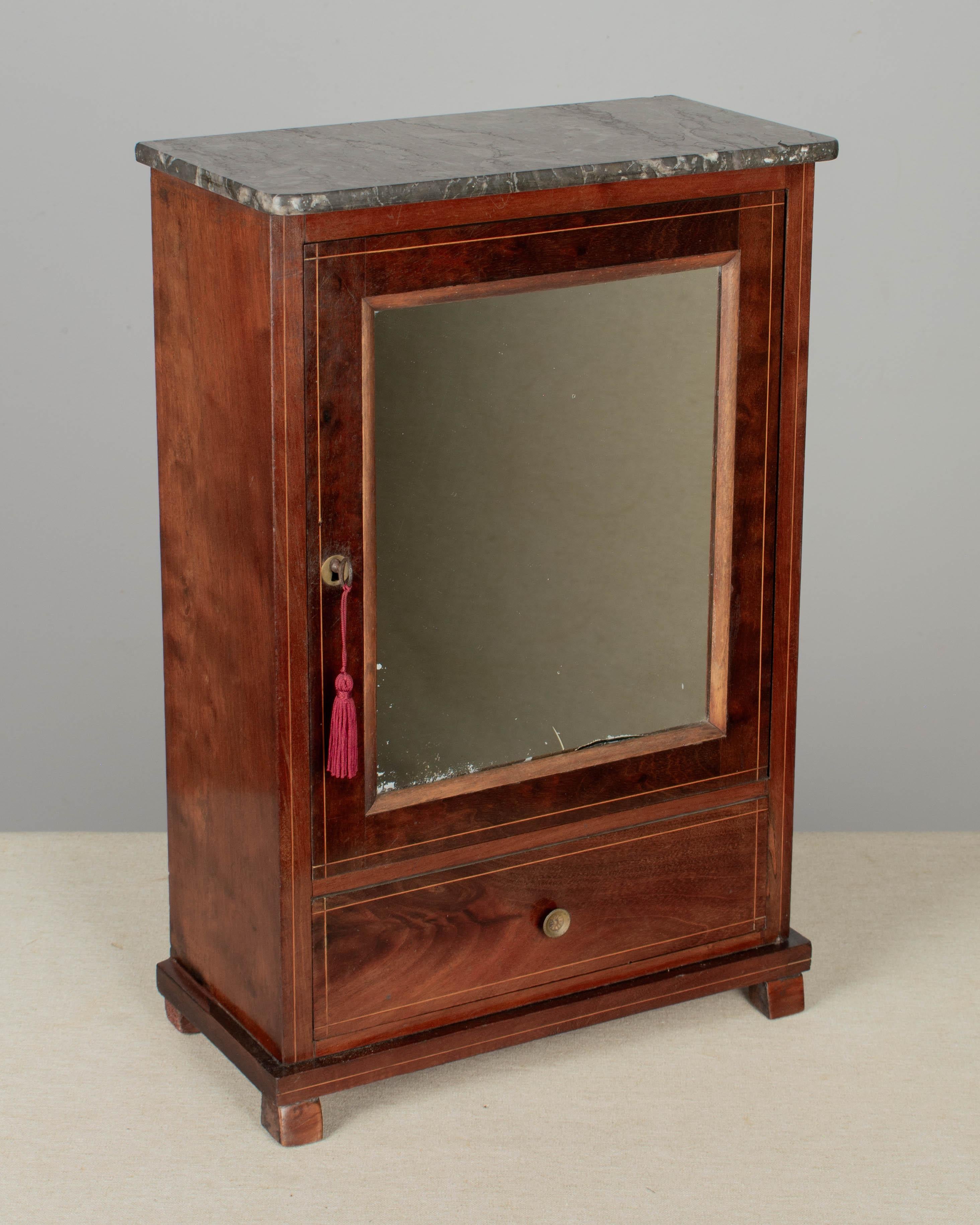An early 20th Century French Louis Philippe style miniature doll armoire. Mahogany veneer with inlay detail and pine as a secondary wood. Mirrored door with drawer below. St. Anne grey marble top. All original. Lock and key are present, but not