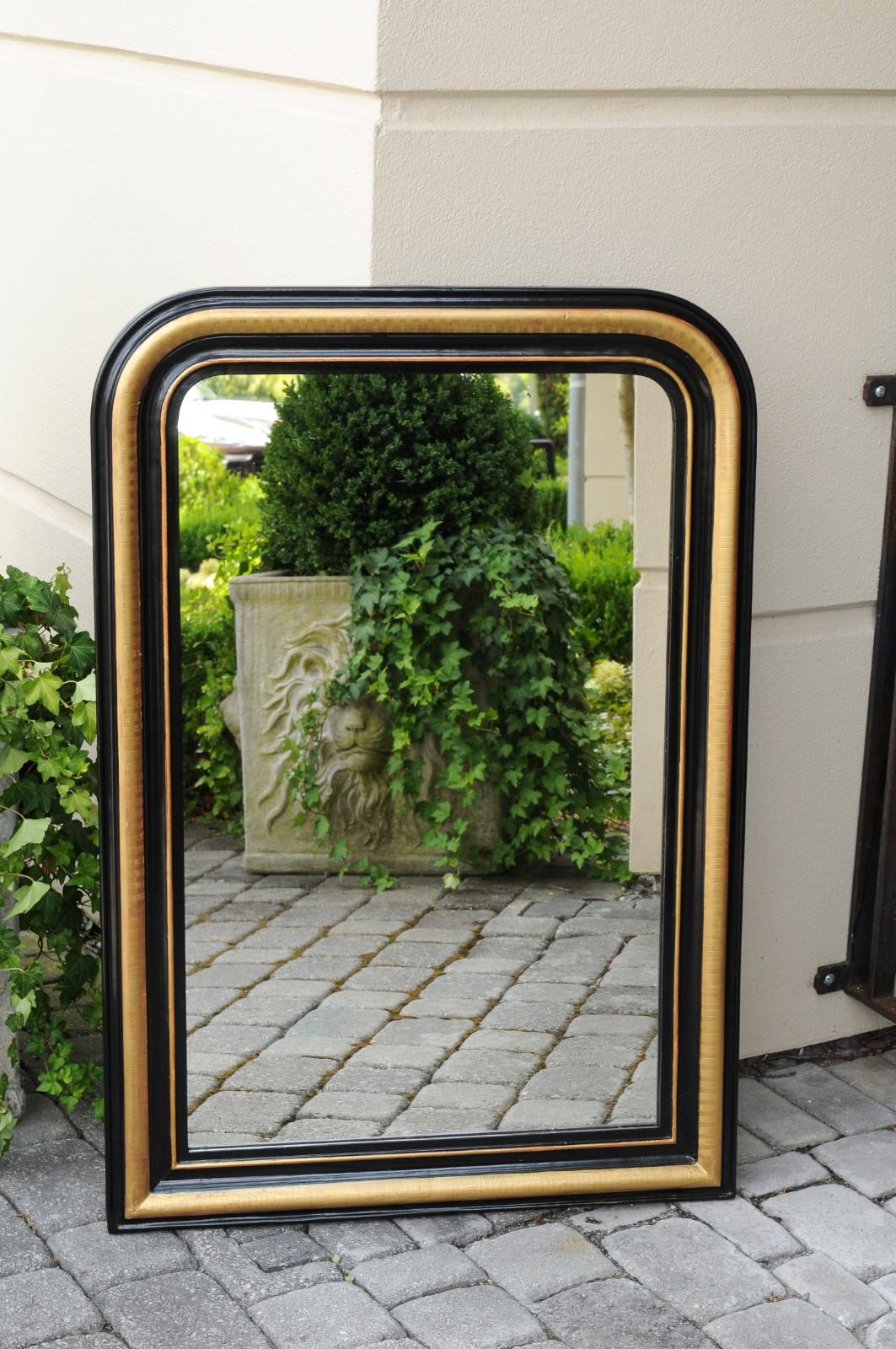 A French Louis-Philippe style wall mirror from the early 20th century, with gilded and ebonized accents. Born in France during the early years of the 20th century, this exquisite mirror presents the stylistic characteristics of the Louis-Philippe