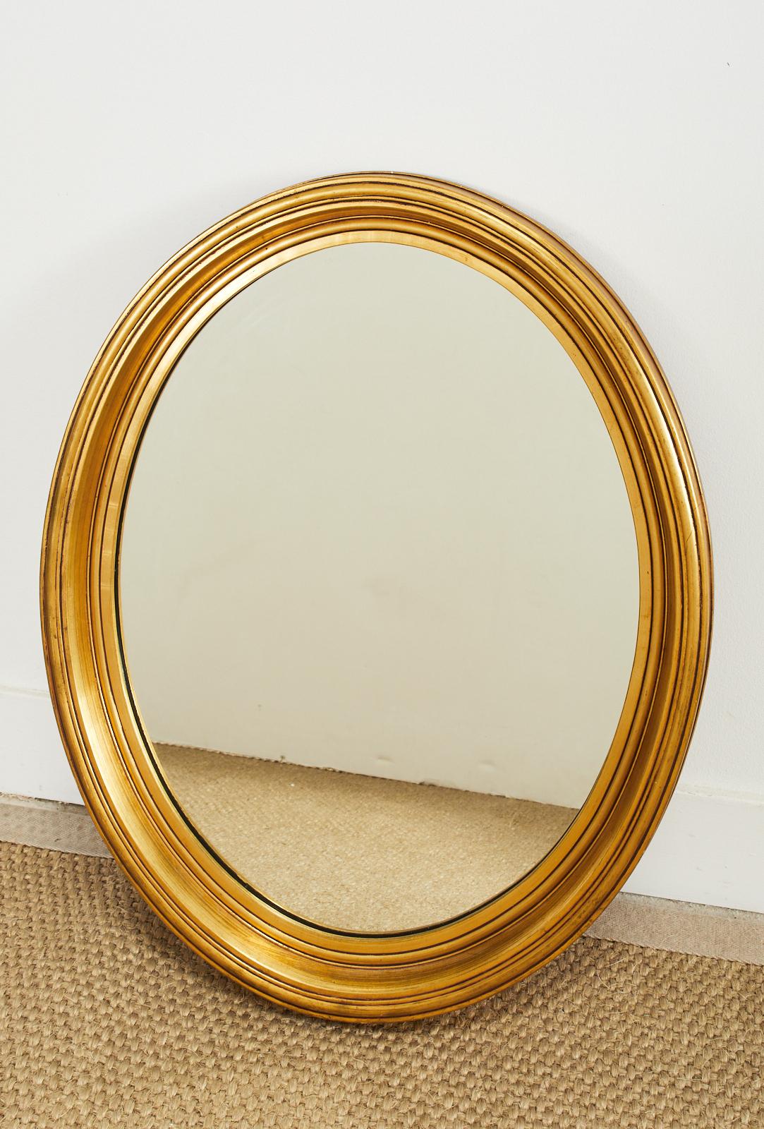 Gorgeous oval giltwood wall mirror crafted in the mid-century by Falconer Plate Glass Co., NYC. The mirror is made in the French Louis Philippe taste with a clean design free from elaborate decoration. The mirror can be hung horizontally or