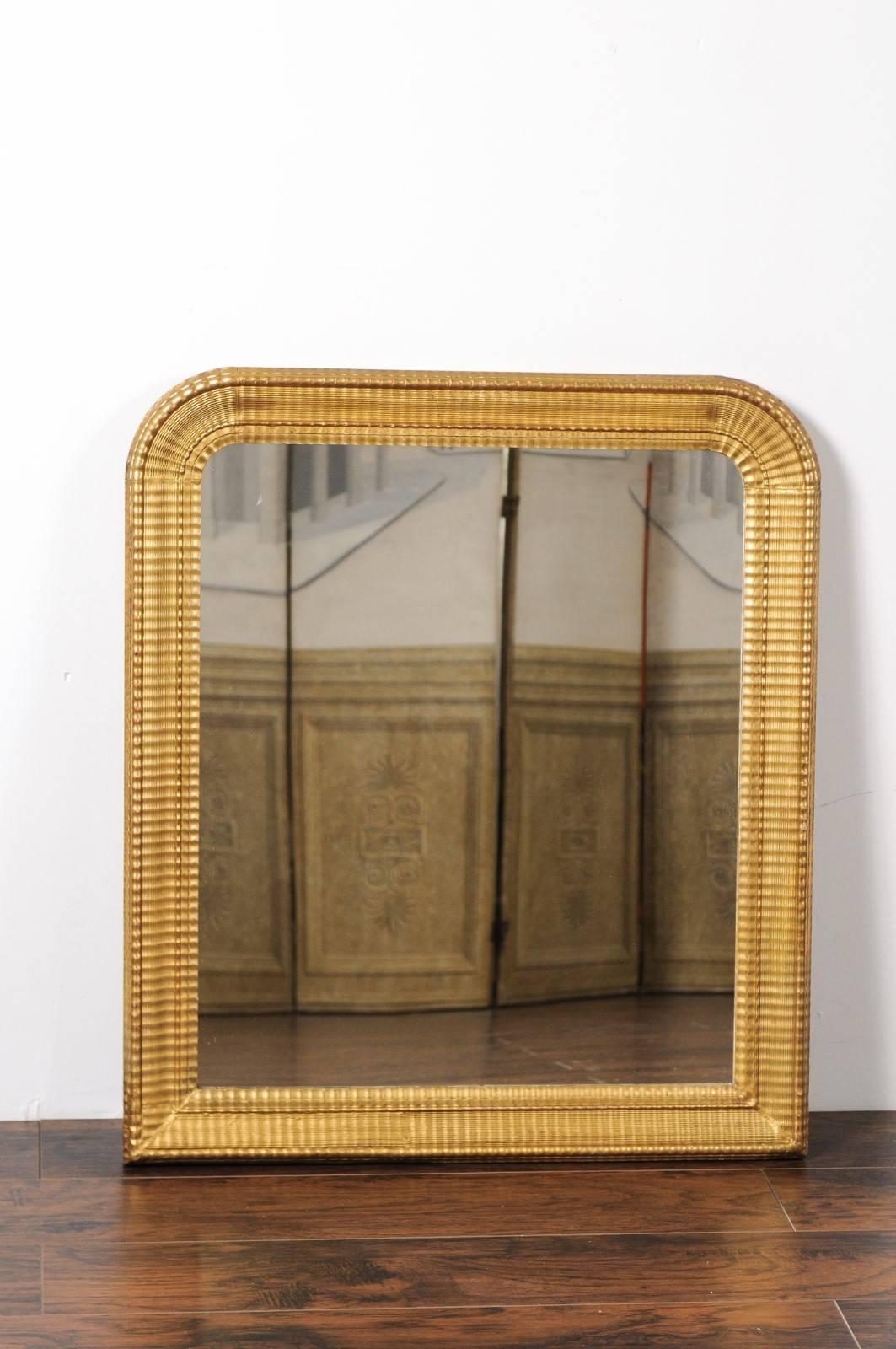A French Louis-Philippe inspired giltwood mirror from the early 20th century with ridged frame. This French mirror features an elegant silhouette, reminiscent of the Louis-Philippe era with its rounded corners at the top. This frame however, is