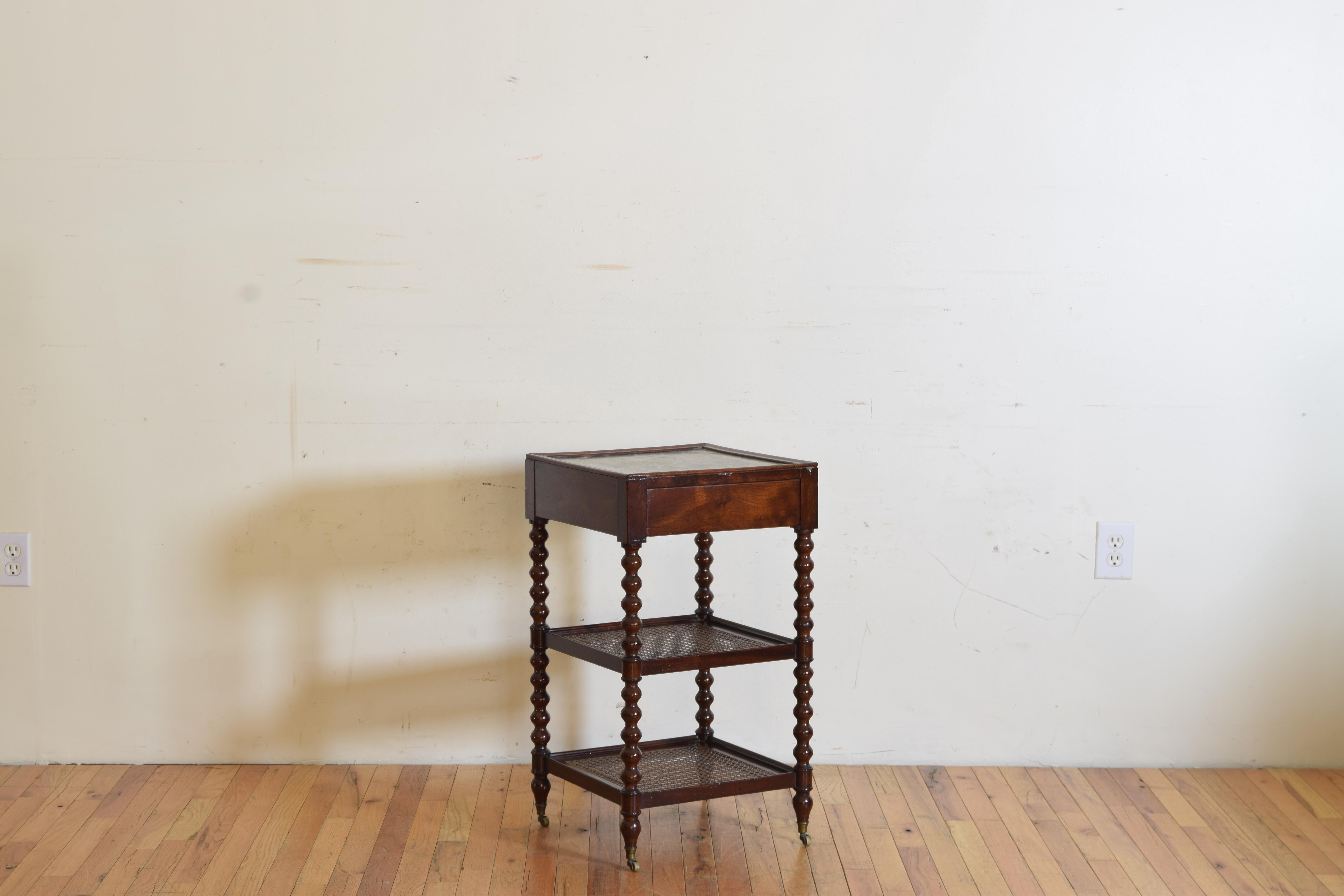 Having a square top with one hidden drawer and a recessed inset marble surface supported by turned legs joined by caned levels, raised on original brass casters, mid-19th century.
