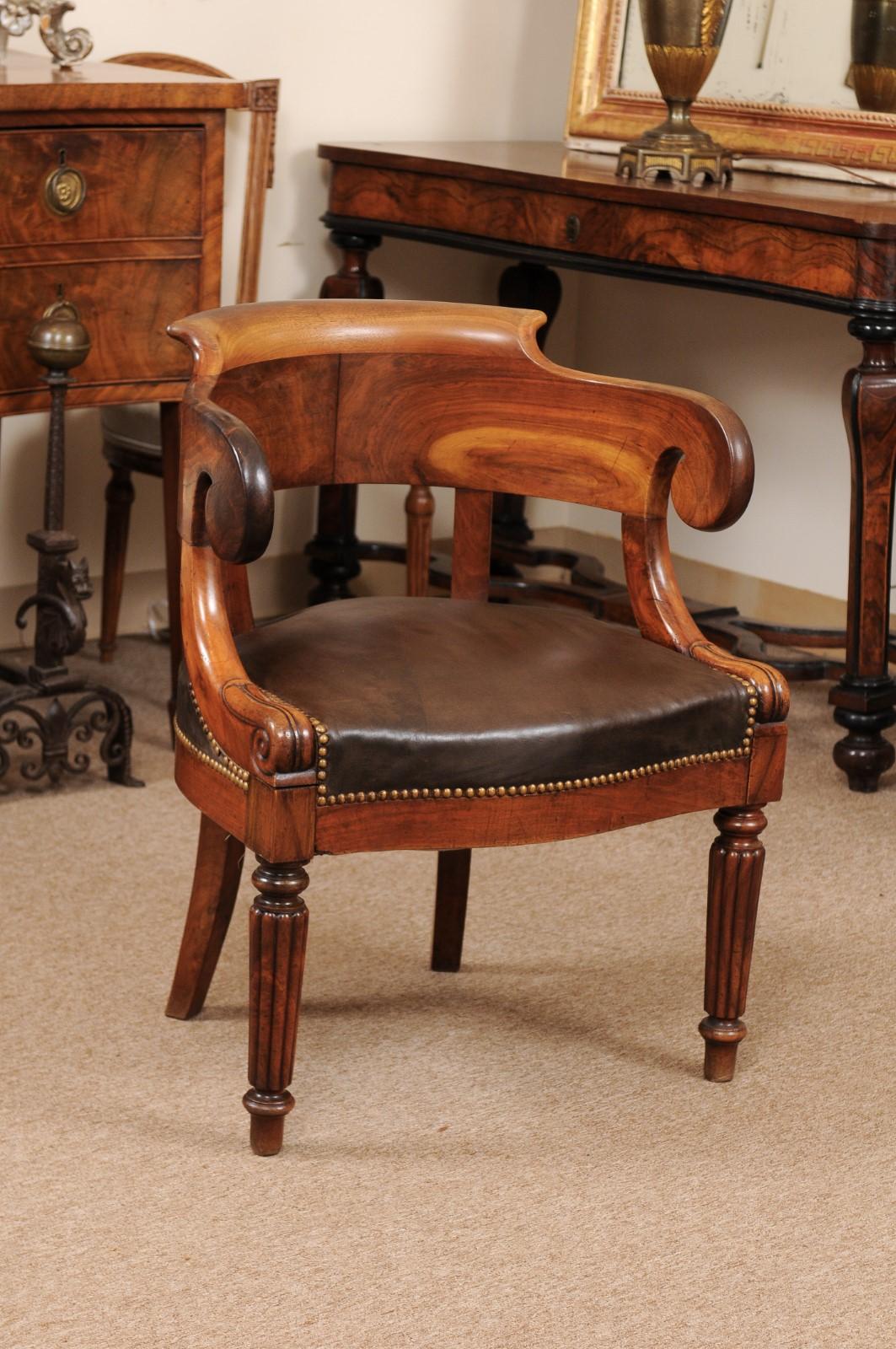 The French Louis Philippe walnut desk chair with rounded back, scroll arms, brown leather seat with brass studded boarder ending in reeded tapered turned legs. 

 
