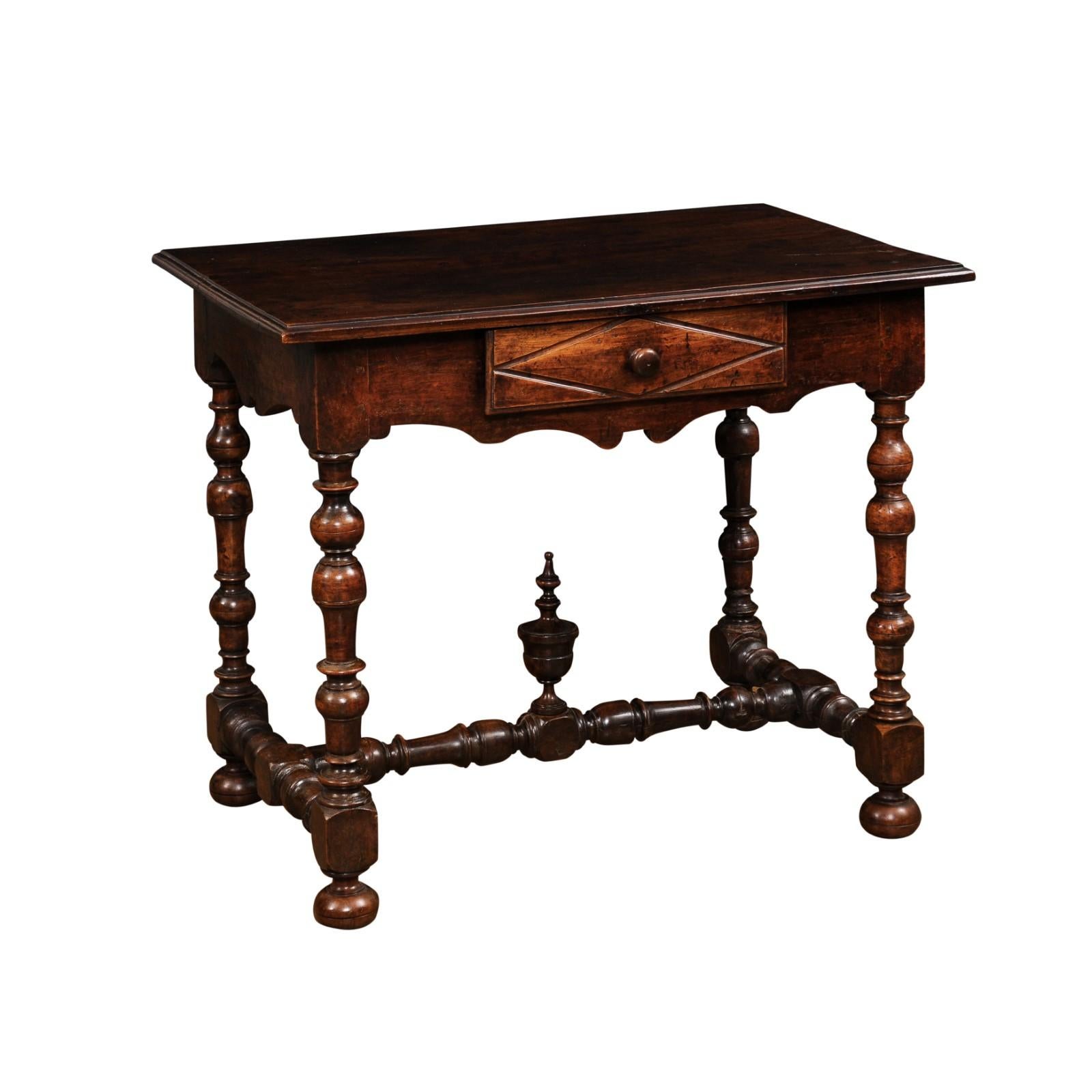 A French Louis XIII period walnut side table from the 17th century, with single drawer, carved diamond motif, turned baluster legs, cross stretcher of similar style with carved finial and mounted on bun feet. This French Louis XIII period walnut