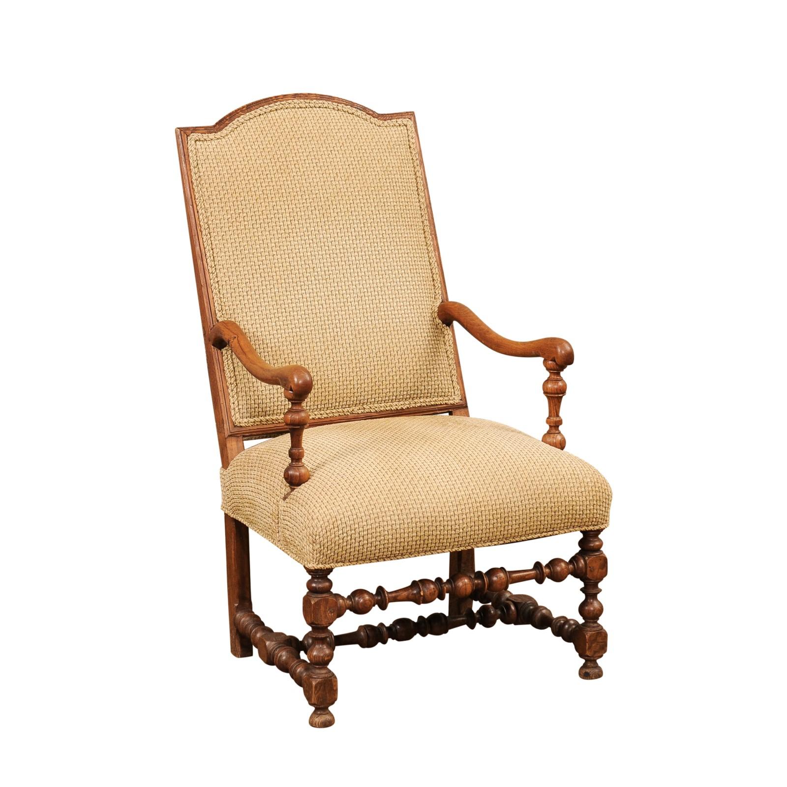 A Louis XIII style French walnut armchair from the 19th century with arched top back, turned base and large scrolling arms. This 19th-century French walnut armchair, crafted in the enduring Louis XIII style, is a testament to timeless elegance and