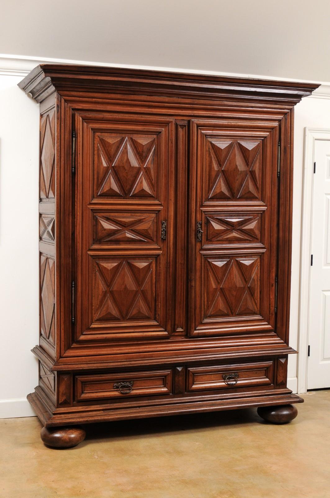 A French Louis XIII style walnut armoire from the 19th century, with raised diamond motifs, doors and drawers. Born in France during the 19th century, this stunning walnut armoire features a molded cornice overhanging a geometric front adorned with