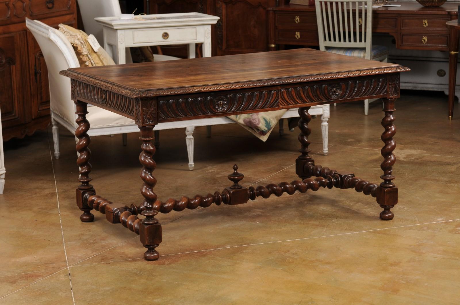 A French Louis XIII style walnut desk from the 19th century, with carved apron, two drawers and barley twist base. Created in France during the 19th century, this walnut desk showcases the stylistic characteristics of the Louis XIII era. The desk