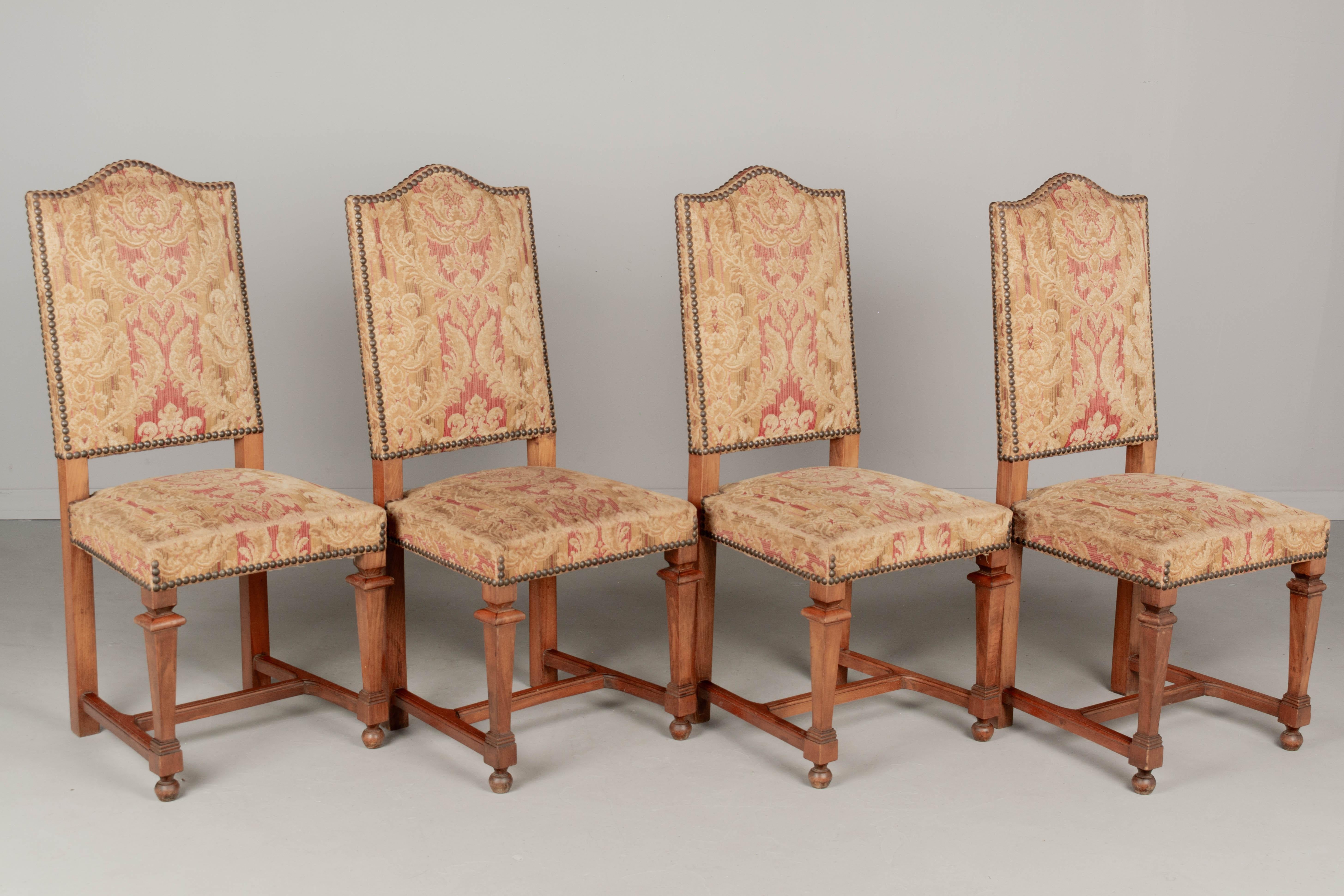 A set of four French Vintage Louis XIII style dining chairs with solid beech wood frames. Original velvet brocade upholstery with nailhead trim. Sturdy and well-constructed with tall backs and stretchers. Fabric is in serviceable condition,