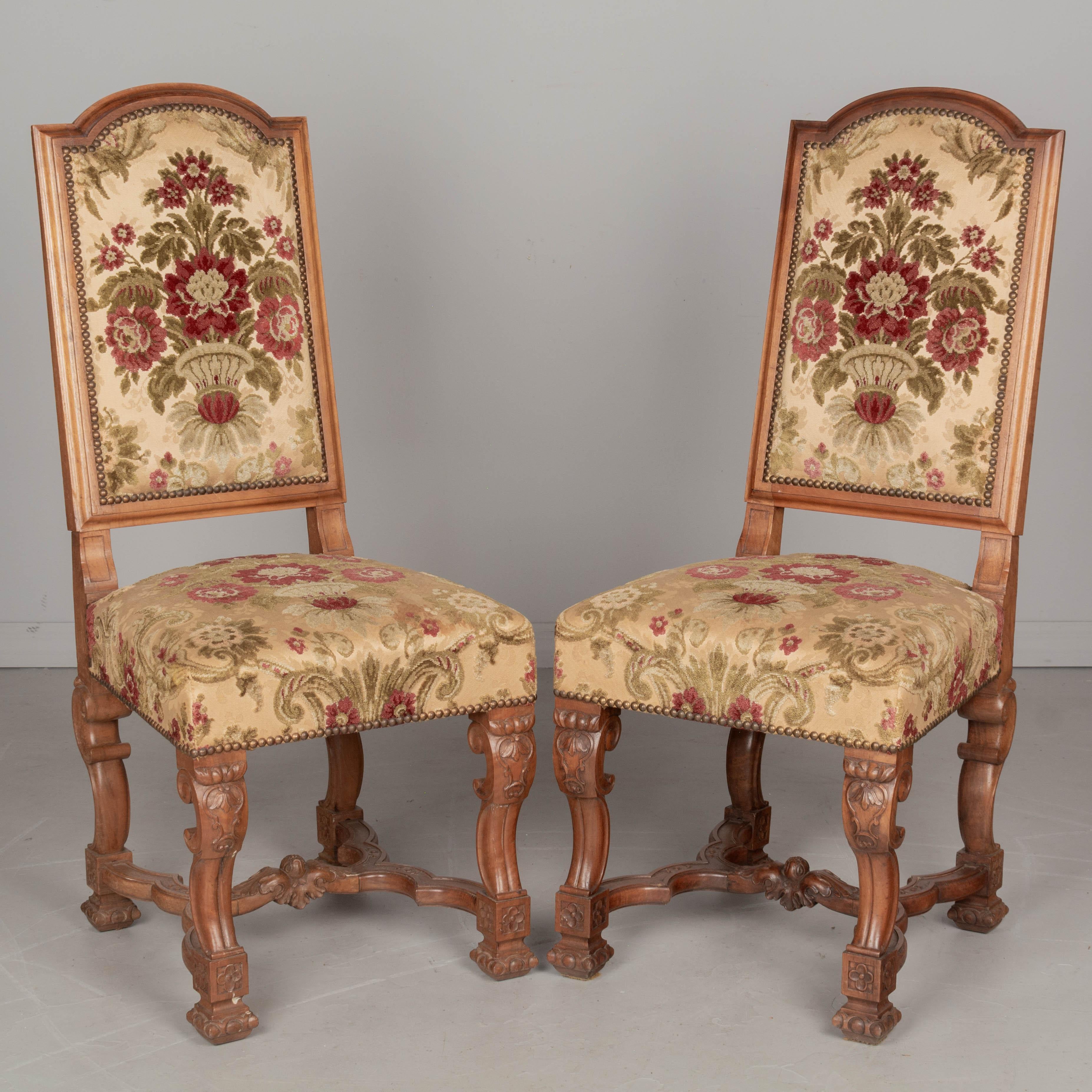 A set of eight French Louis XIII style dining chairs with solid walnut frames and original velvet brocade upholstery. Sturdy and well-constructed with tall back, carved legs and stretchers. Fabric is in good condition, with the exception of two