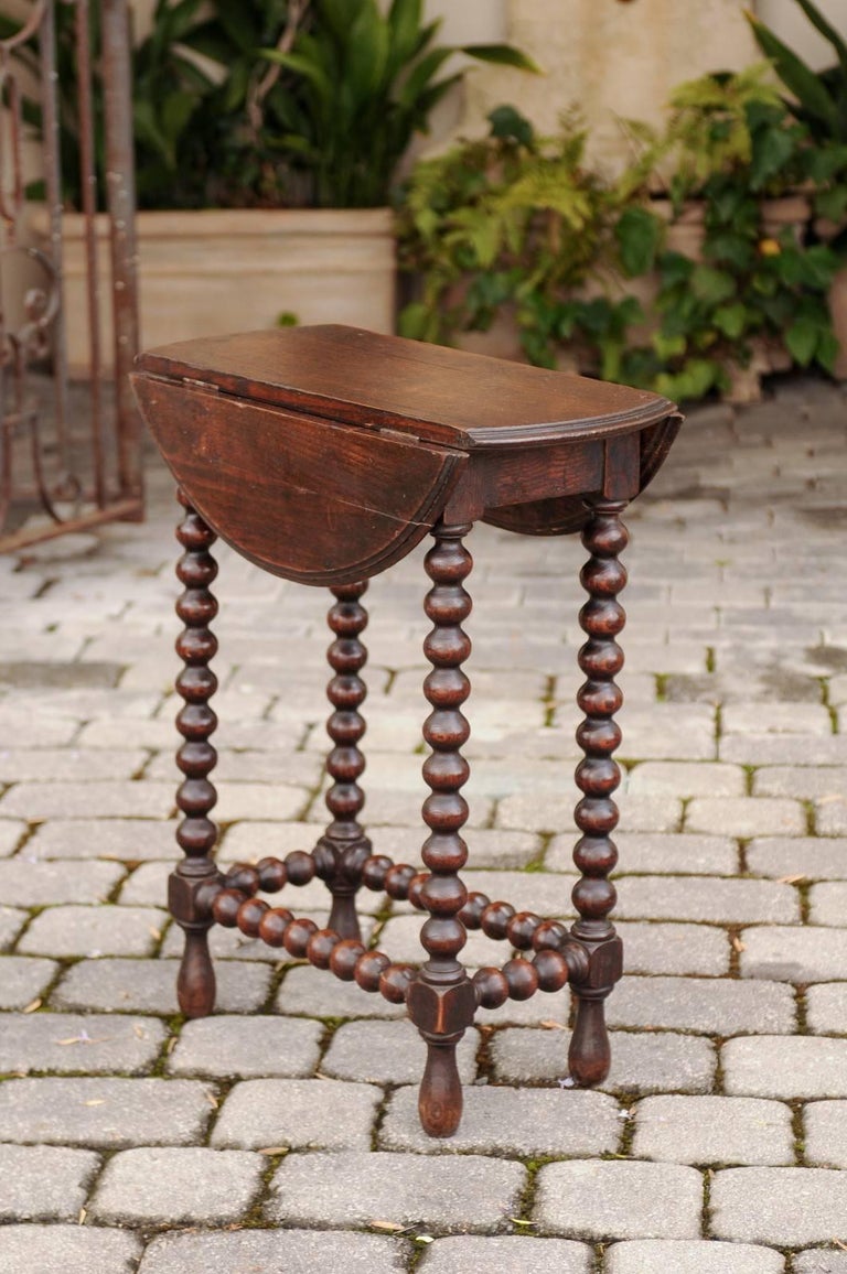 A petite French Louis XIII style oak drop-leaf bobbin leg table with swivel top from the late 19th century. This small French side table features a drop-leaf top that swivels to open fully, revealing a circular shape. The table is raised on an