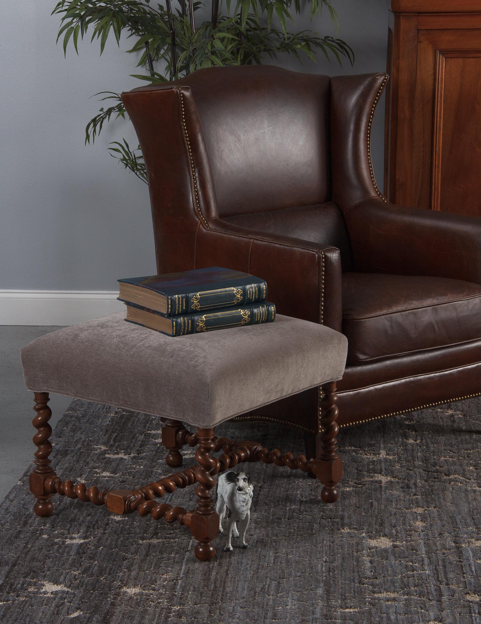 A large vintage Louis XIII style walnut ottoman in taupe upholstery from France, circa 1920s. The rich brown walnut frame has elegant barley twist construction with a sturdy H-stretcher and block die joints. Round bun feet with incised lines for