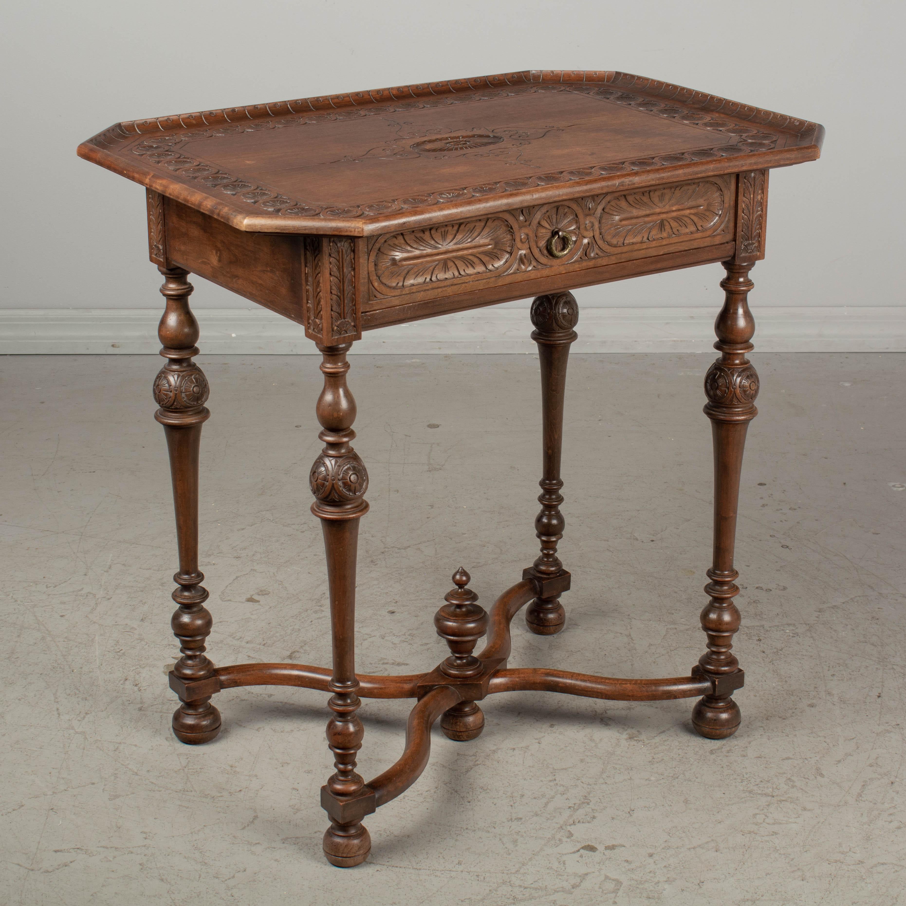 A Louis XVIII style French side table made of solid walnut with carved decoration. Dovetailed drawer with small brass ring pull. Turned legs connected by an X-form stretcher with center finial. Pegged construction. Waxed patina. 
 

 