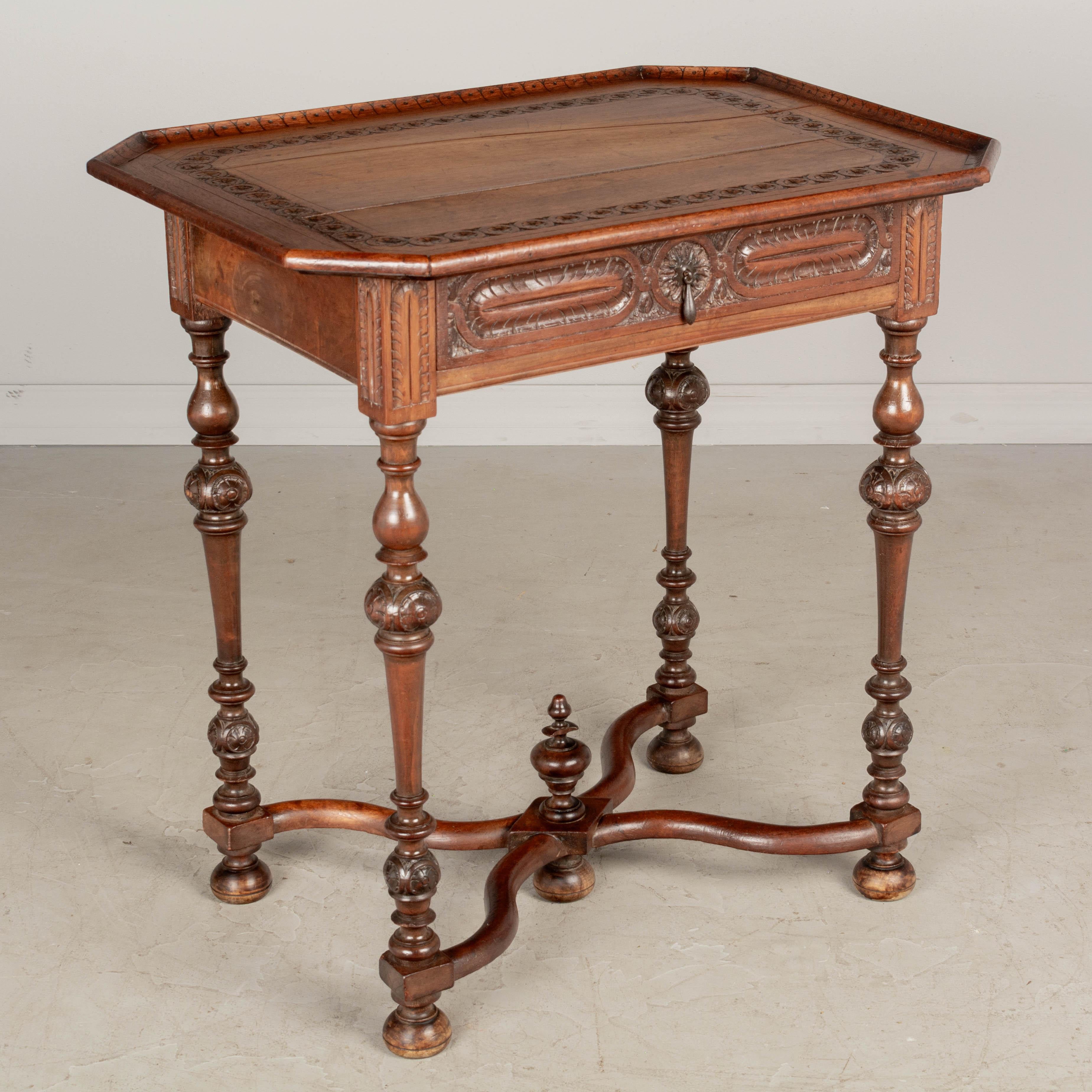 A Louis XVIII style French side table made of solid walnut with carved decoration. Dovetailed drawer with small pull. Turned legs connected by an X-form stretcher with center finial. Pegged construction. Waxed patina. Circa 1920-1940. Dimensions: