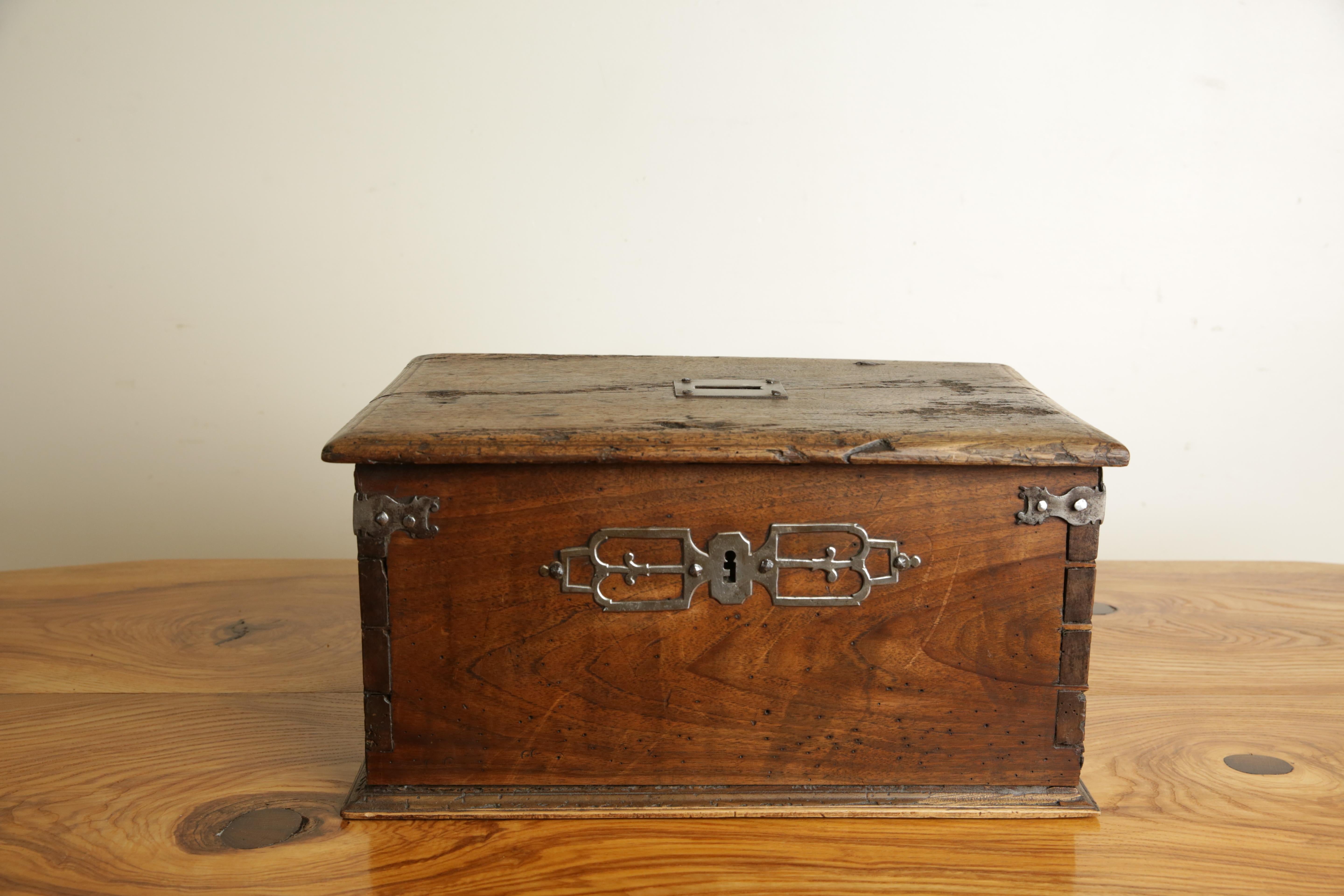 Il piano rettangolare con un bordo modellato e una linea intagliata al centro con una fessura per le monete, la cassa conforme con cinghie di rinforzo in acciaio e una rosetta decorativa in acciaio, con serratura originale.