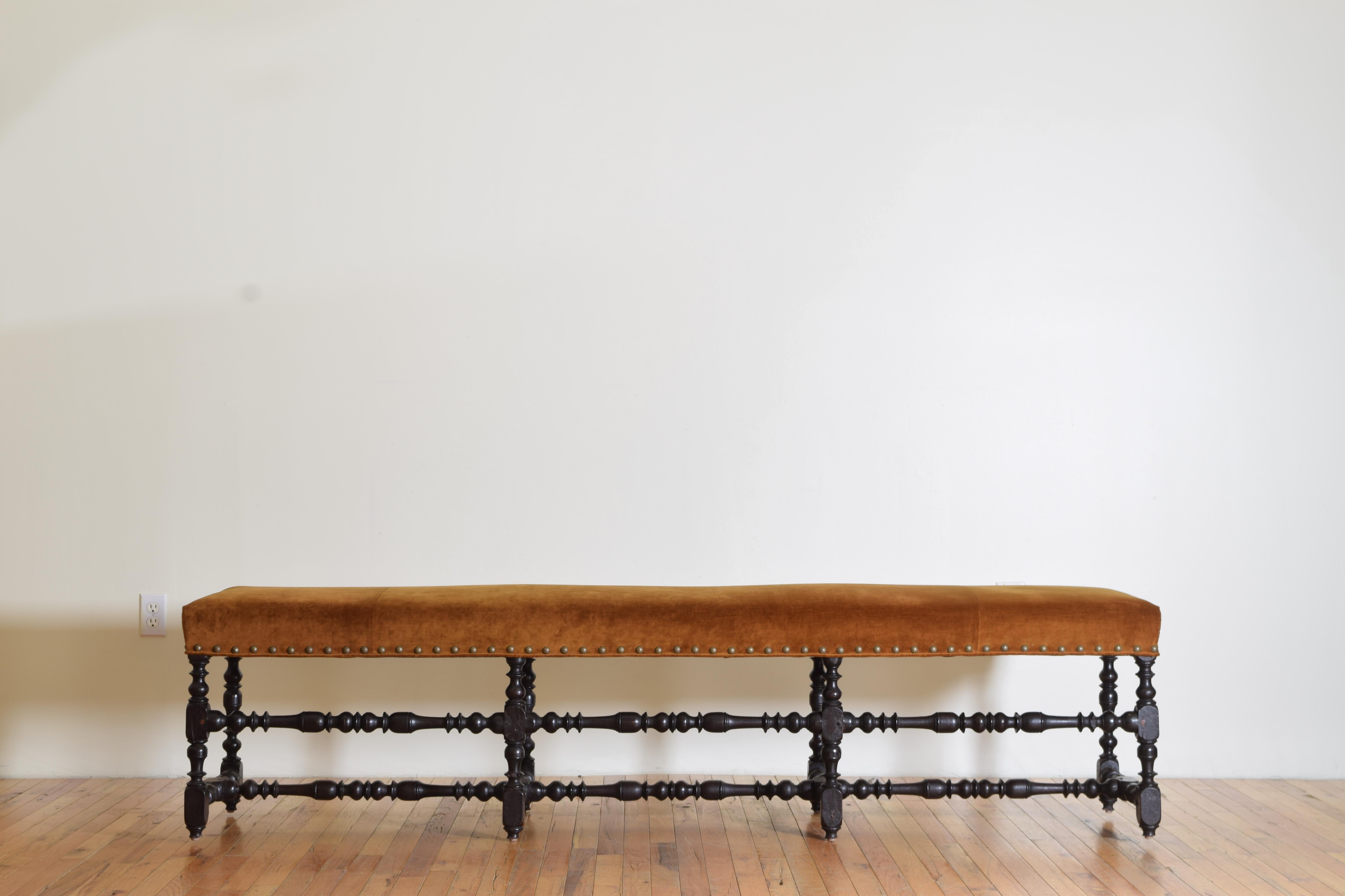 Unusual in length this bench is upholstered in a rich brass nailhead trimmed velvet, the frame of the bench has 8 turned legs with block feet joined by a triple h-form turned stretcher, the front of the bench with a mid-rise turned stretcher.