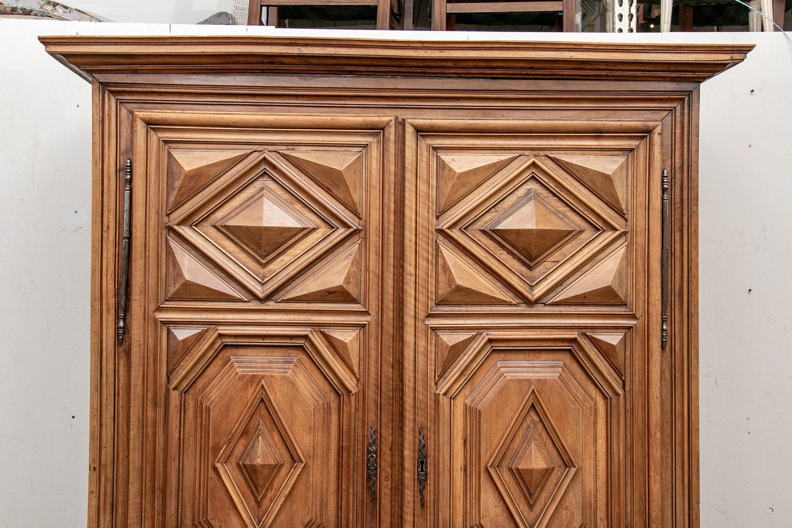 A carved cornice over elaborately carved double doors with high relief diamond shaped panels. Carved side panels and lower frame, raised on large bun feet. Metal hardware with one escutcheon (lacking a key). Inner supports for three shelves, one