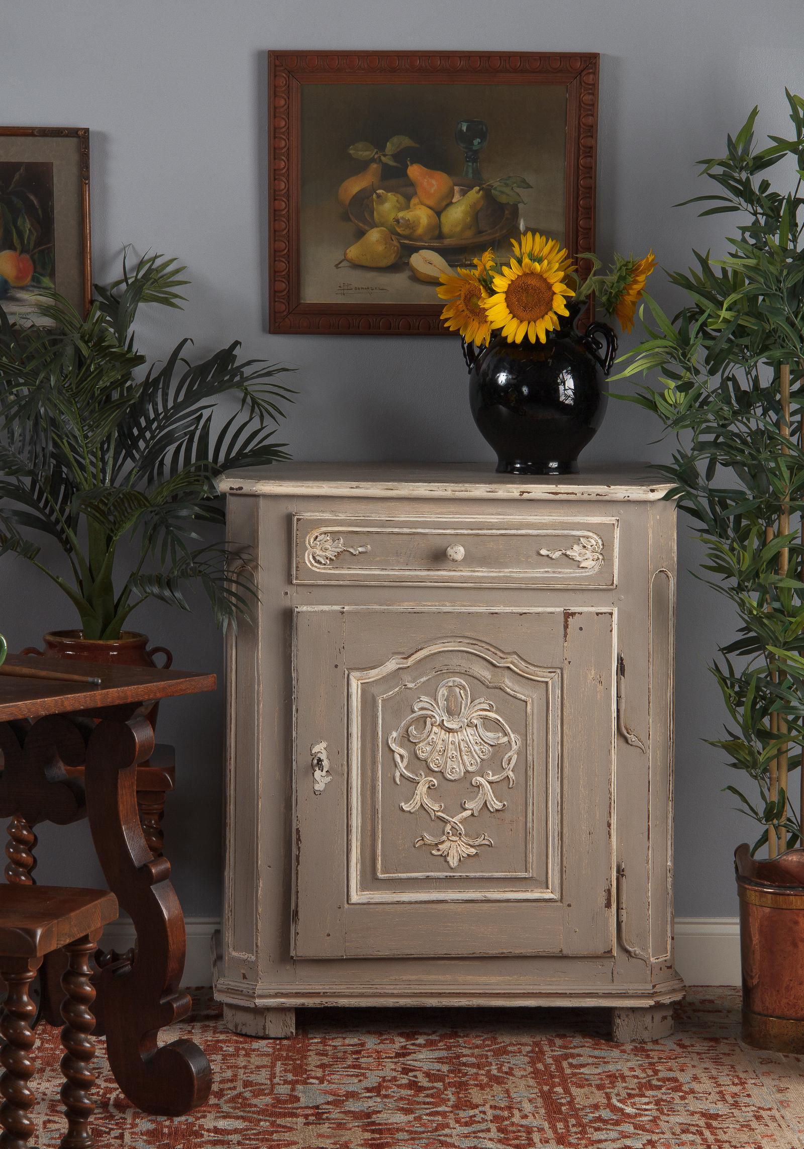 A charming oak painted Louis XIV confiturier or preserves cabinet, French 18th century. Distressed light gray paint with cream highlighting the decorative details. Paneled sides and canted front corners, a single drawer on top with a single door